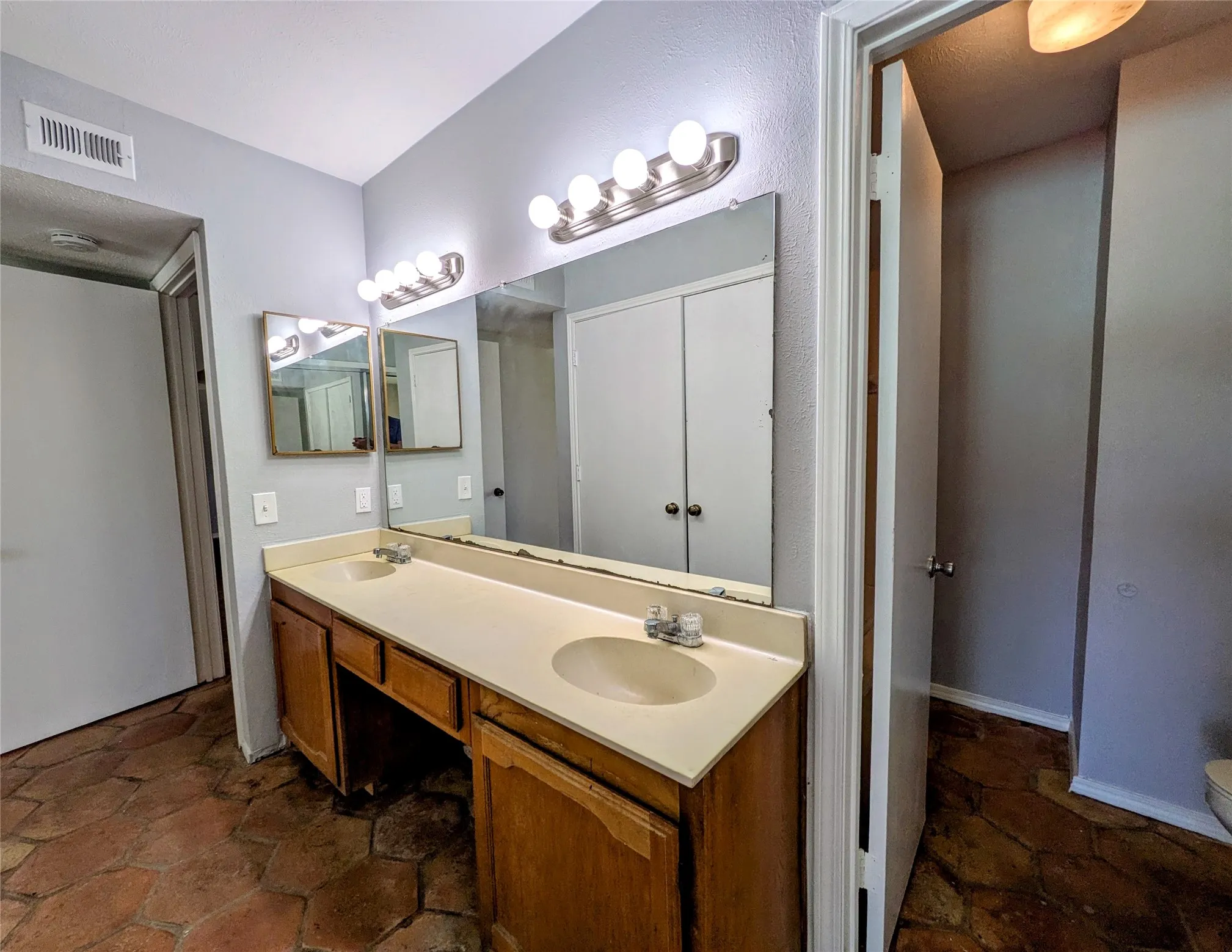 Dual basin vanity with a laminate countertop, wood-finish cabinetry, and sconce lighting