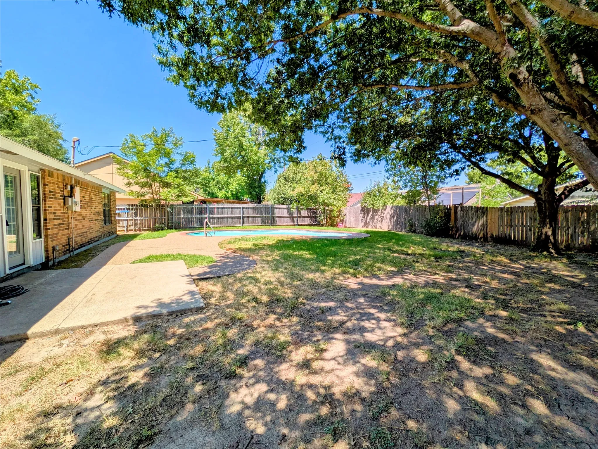 Spacious backyard featuring a large swimming pool, concrete patio, privacy fencing, and mature trees