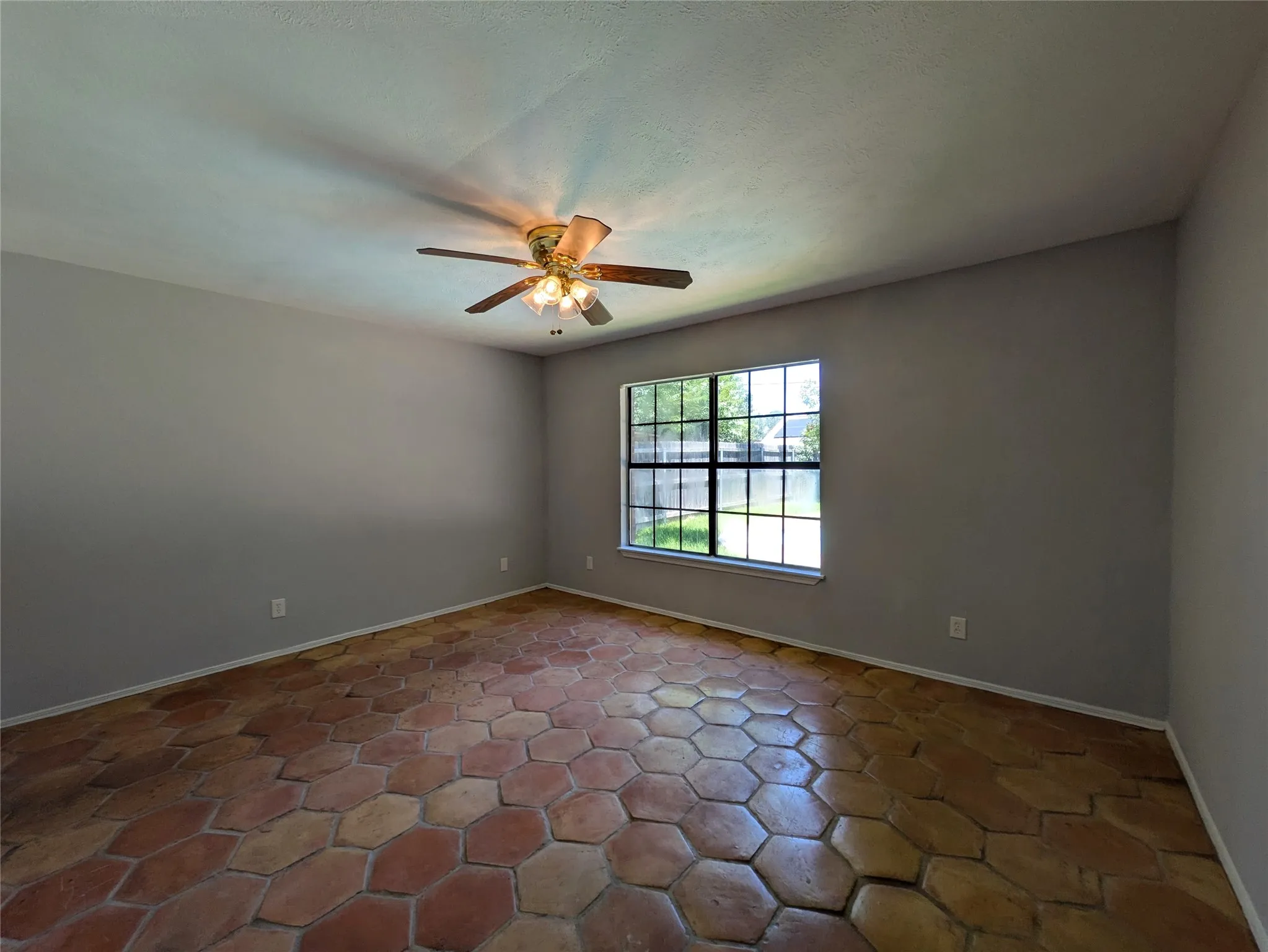 Hexagonal terra cotta tile flooring, a multi-pane window with exterior views, and a ceiling fan with integrated lighting
