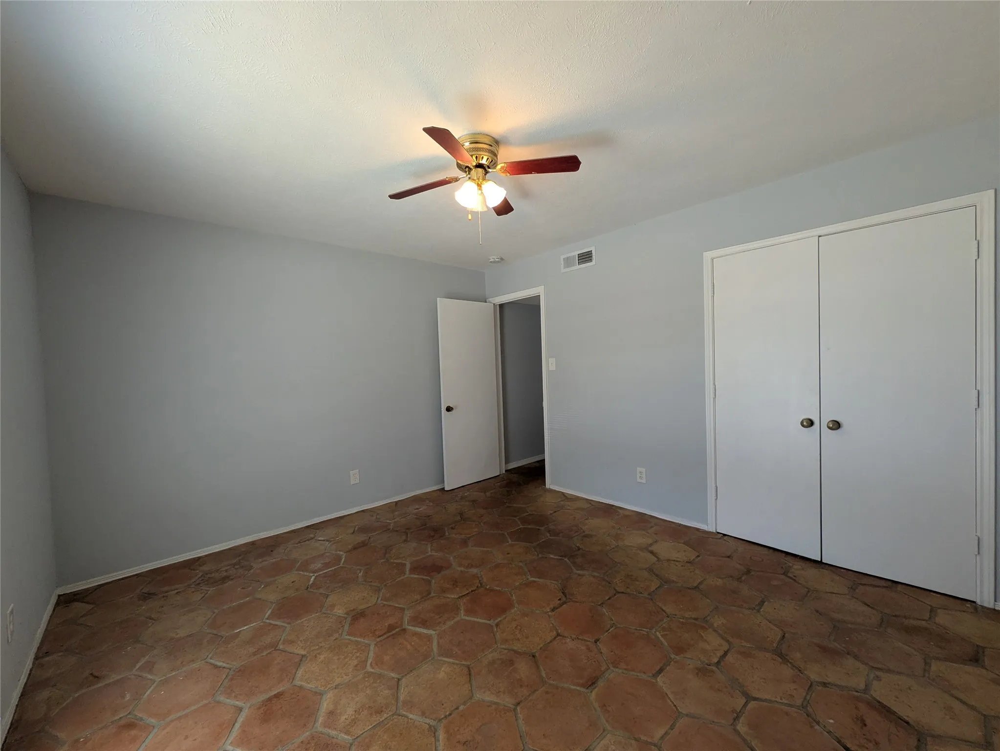 Hexagonal tile flooring, ceiling fan with integrated lighting, light-toned wall paint, and white bi-fold closet doors