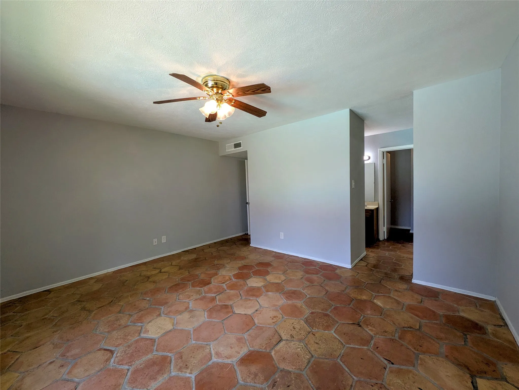 Hexagonal terracotta tile flooring, ceiling fan with integrated lighting, and a neutral wall color