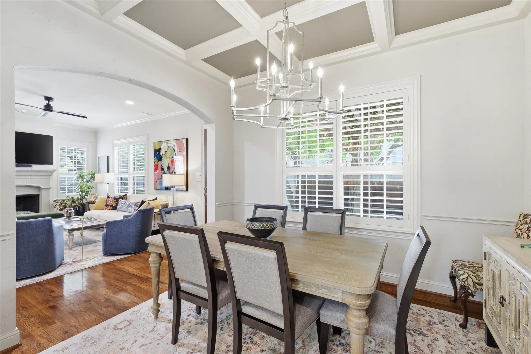The large dining room has beautiful lighting and coffered ceilings with plantation shutters and views of the front courtyard
