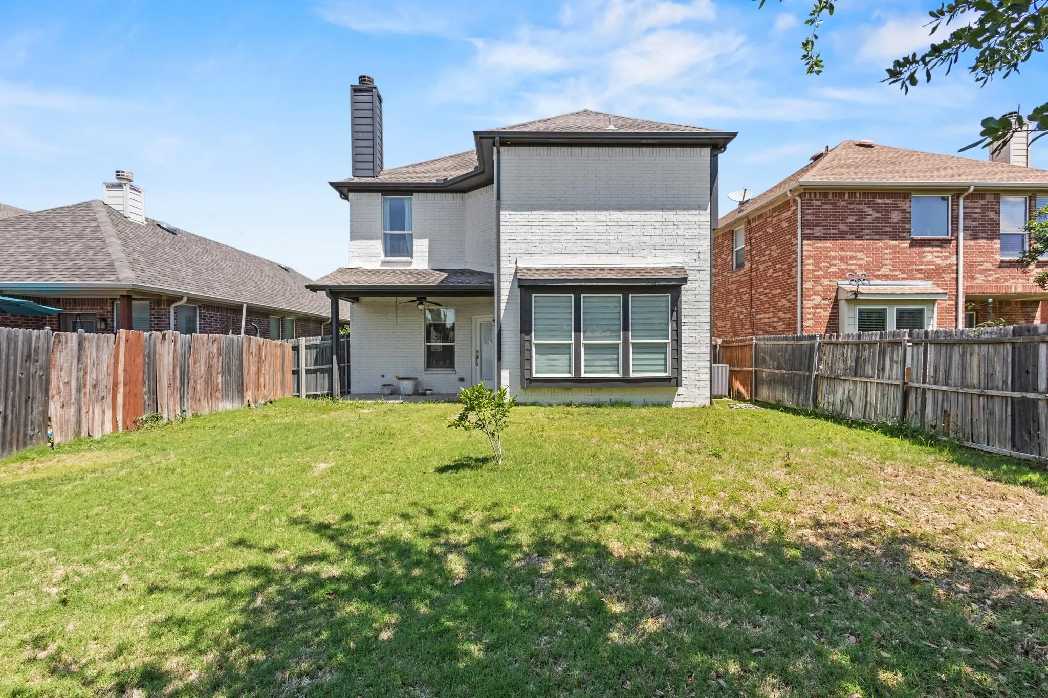 Expansive rear yard with a manicured lawn, full privacy fencing, and a covered patio with a ceiling fan
