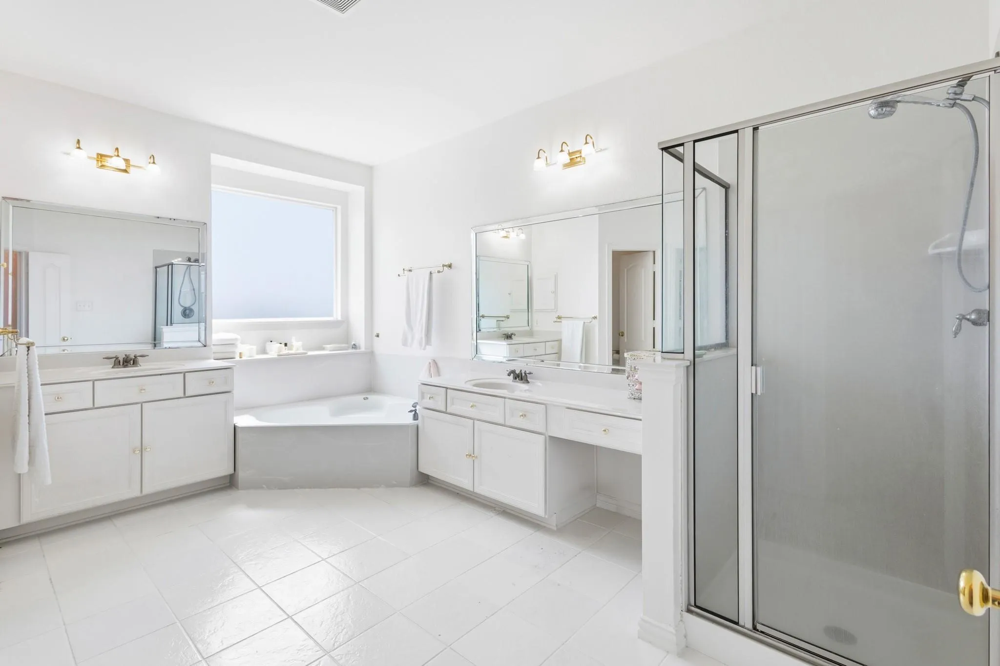 Spacious bathroom featuring a built-in tub, dual vanity areas, glass-enclosed shower, and tiled flooring