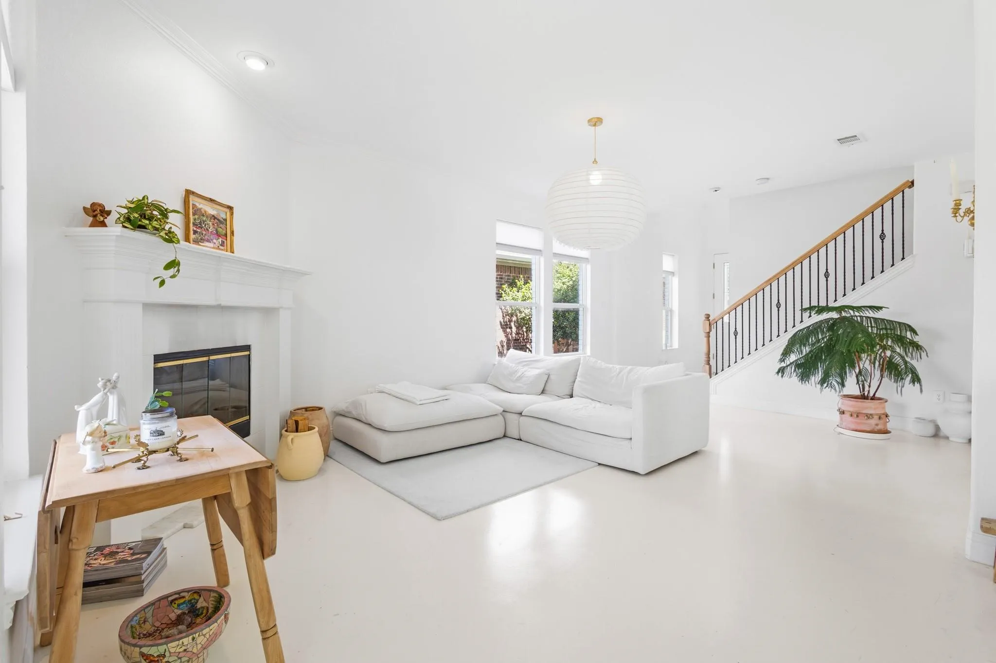 White-painted flooring, fireplace with mantel and glass doors, staircase with wooden handrail and black balusters, and recessed ceiling lighting