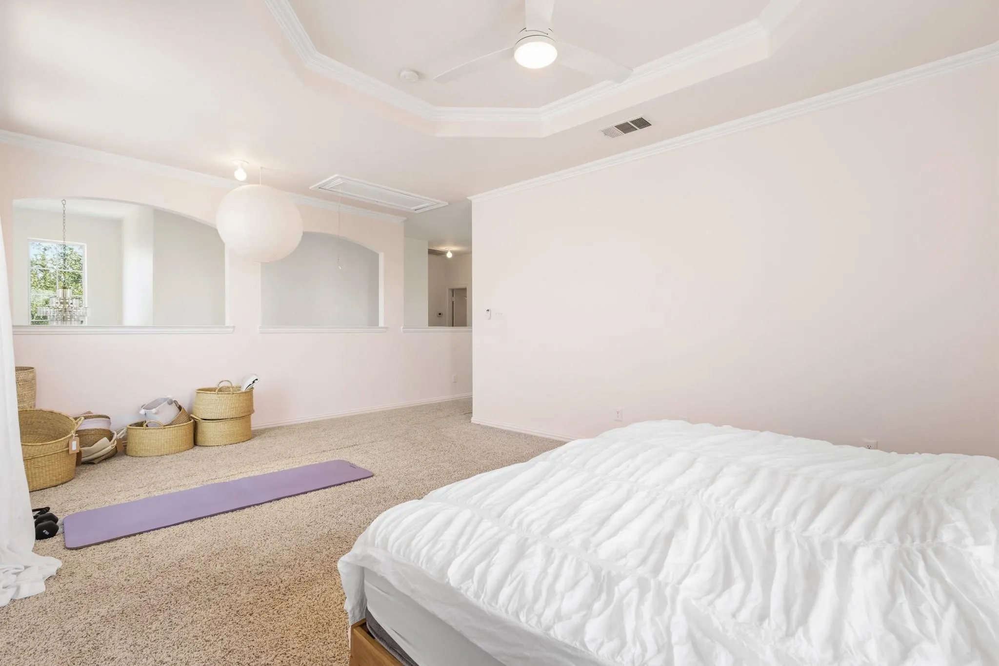 Tray ceiling with crown molding, ceiling fan with integrated lighting, carpeted flooring, and architectural arched wall openings