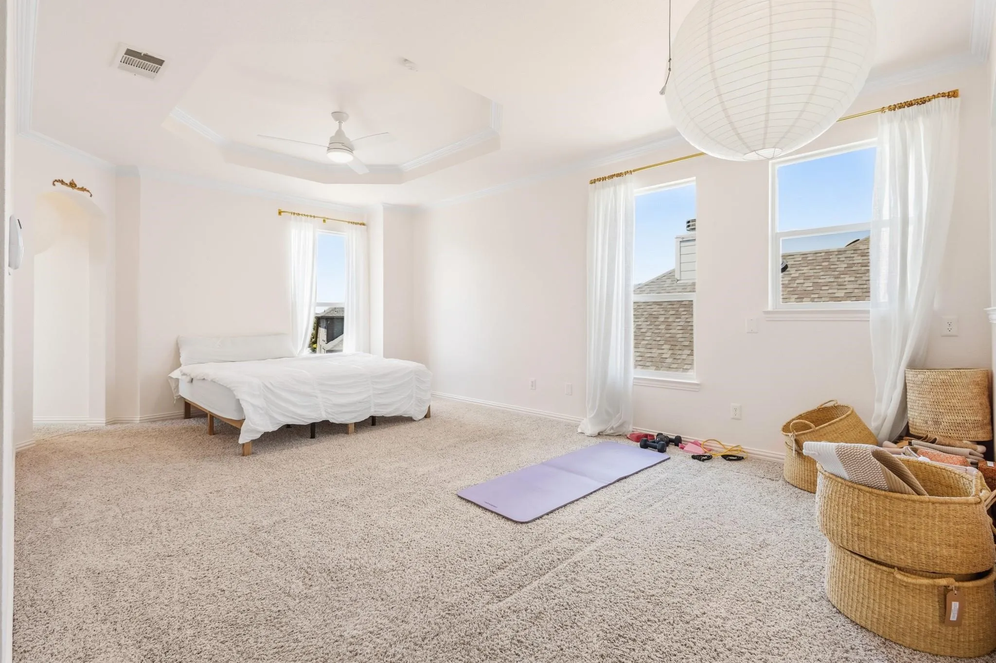 Recessed tray ceiling with crown molding, ceiling fan, plush carpeting, multiple windows, and a built-in wall niche