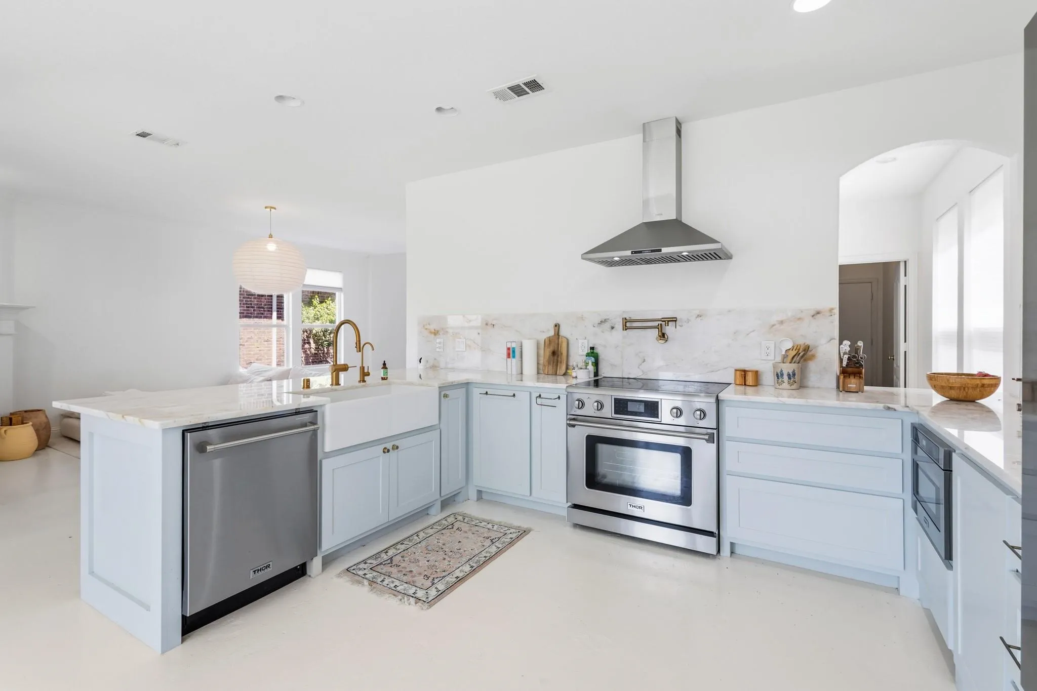 Kitchen featuring light-toned cabinetry, stainless steel appliances, a farmhouse sink, and light-toned countertops