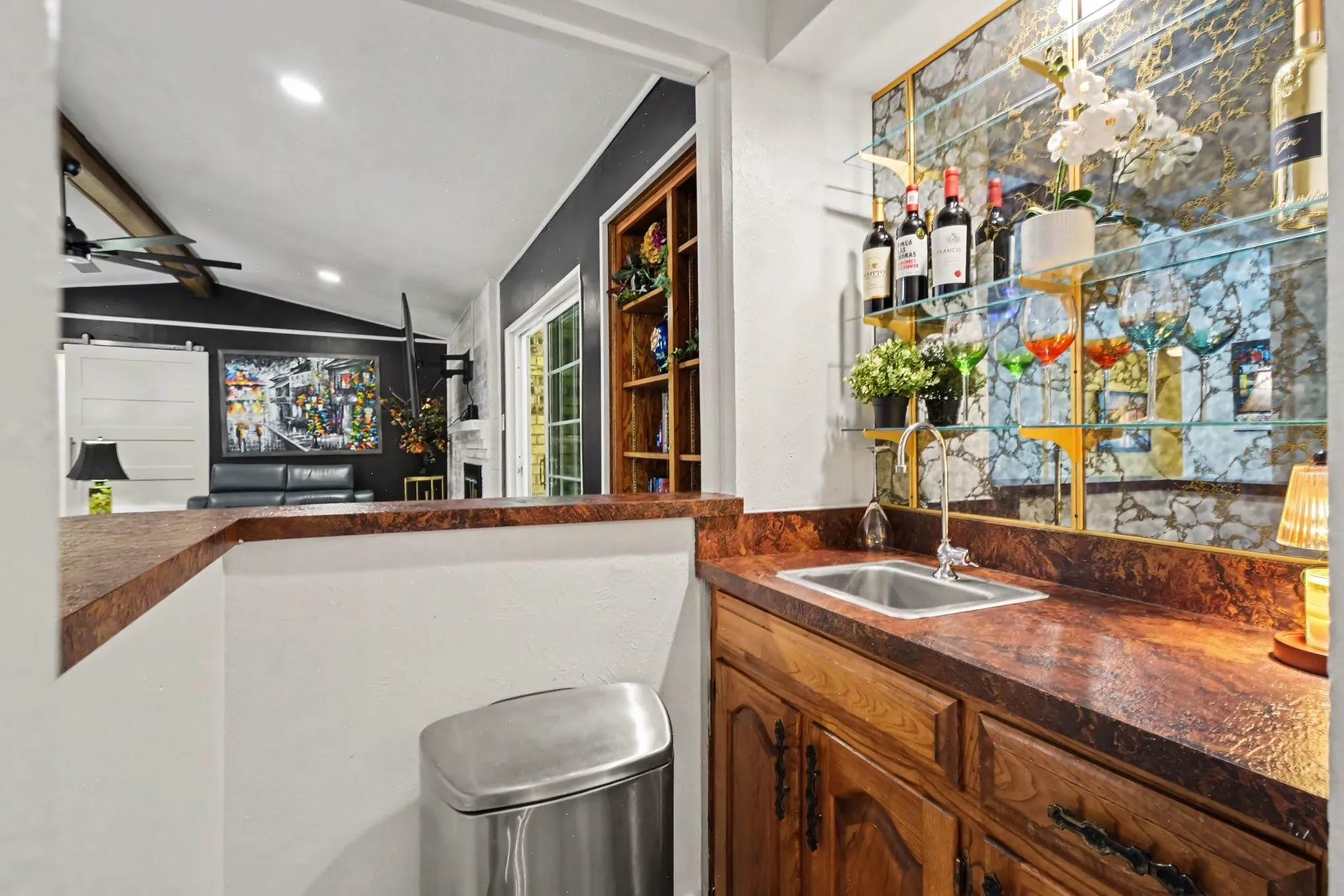 Wet bar with a stainless steel sink, wood-finish cabinetry, and glass shelving