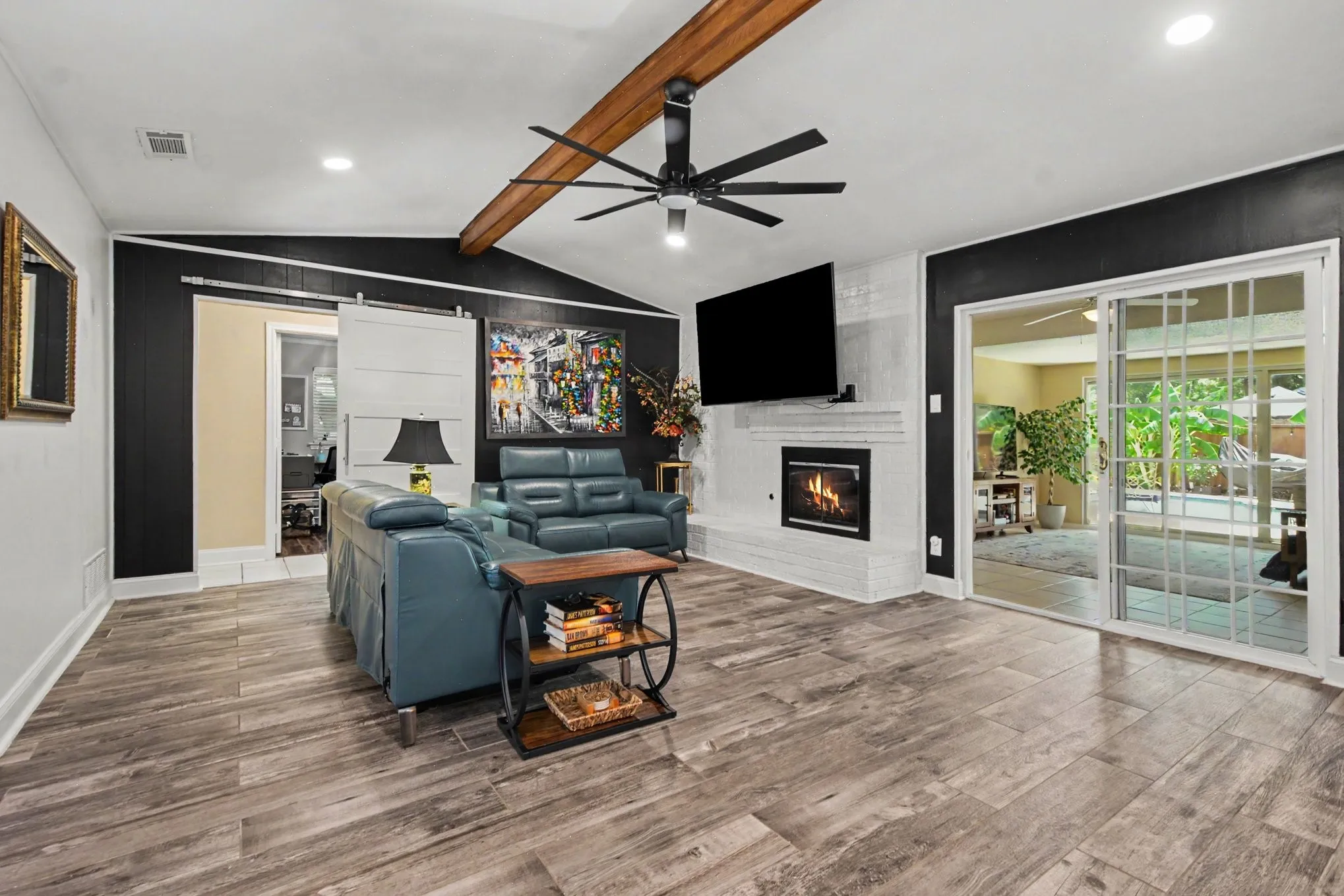 Vaulted ceiling with exposed wood beam, wood-finish flooring, fireplace, sliding glass door, and a barn door