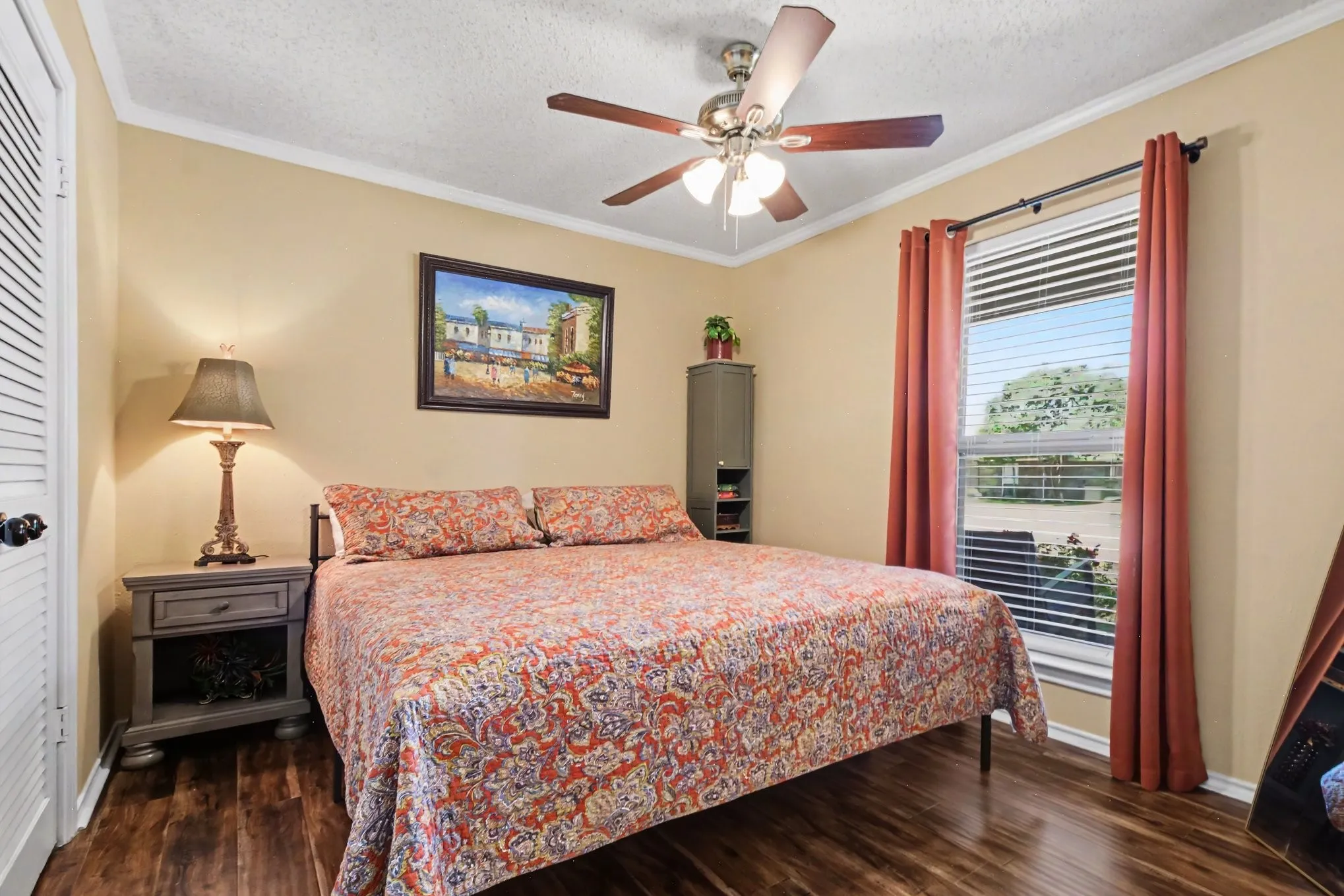 Wood-finish flooring, ceiling fan with integrated lighting, window with blinds, crown molding, and a built-in closet with louvered doors