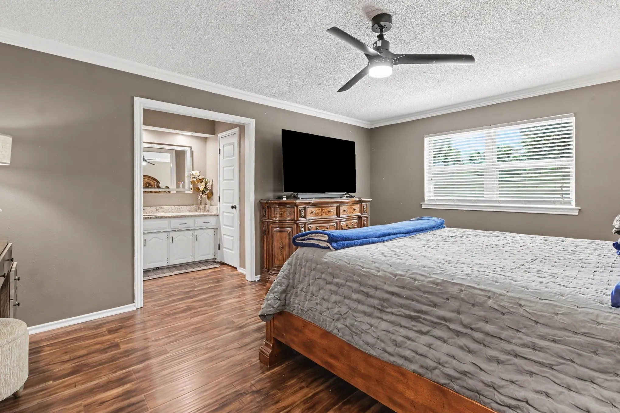 Wood-finish flooring throughout, crown molding, ceiling fan, and a window with blinds