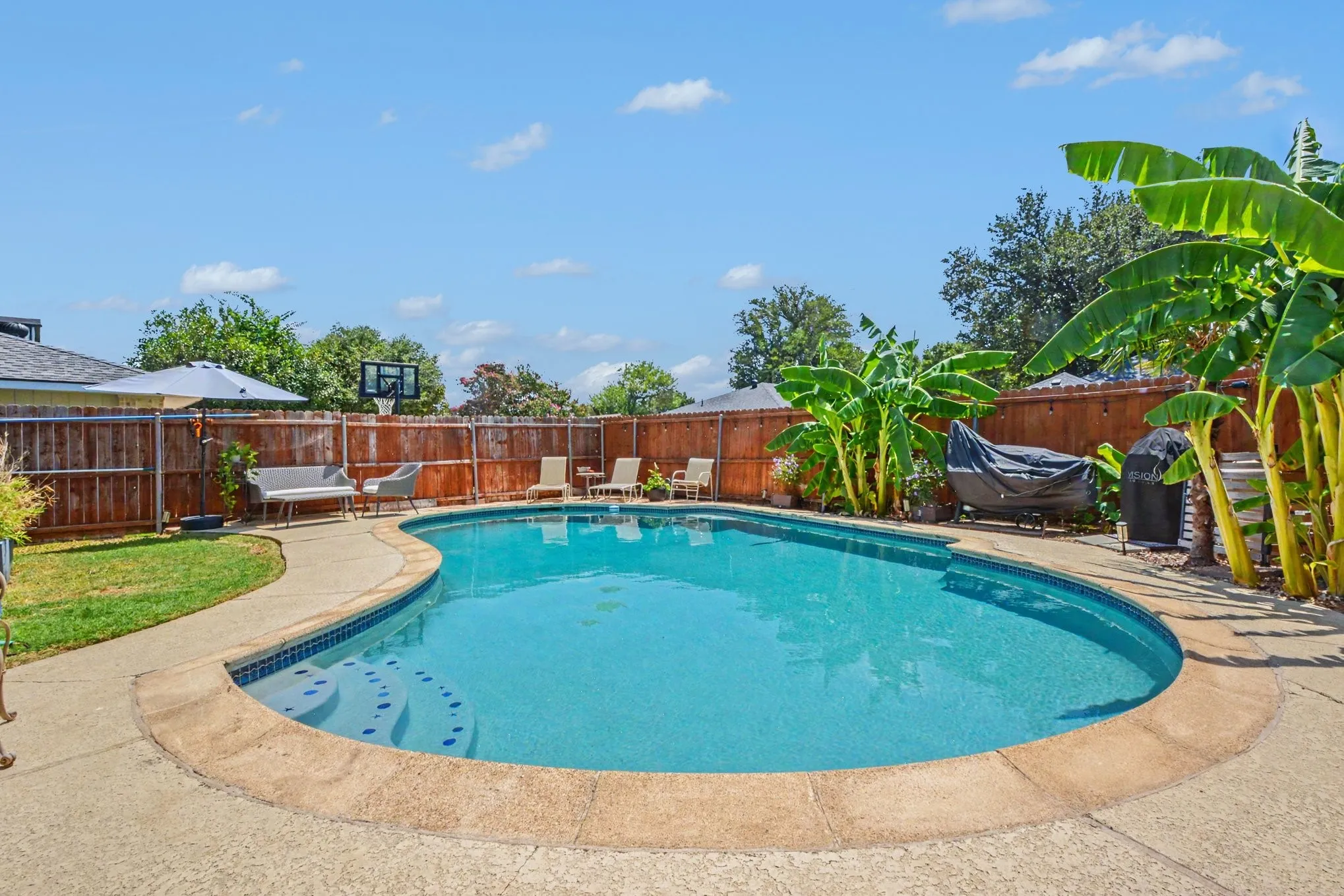 In-ground swimming pool featuring a curved concrete deck, integrated steps, and blue tile accents