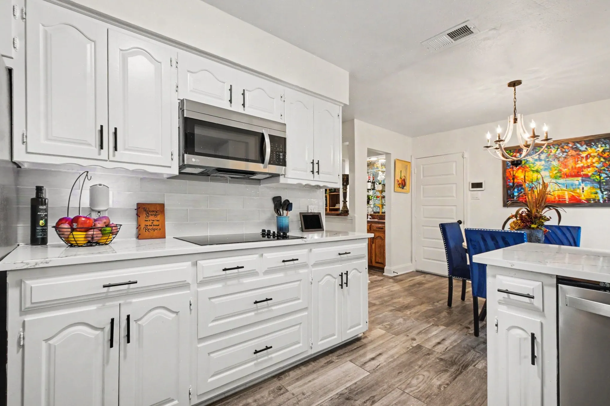 White cabinetry with matte black hardware, stainless steel microwave, integrated cooktop, subway tile backsplash, and wood-finish flooring