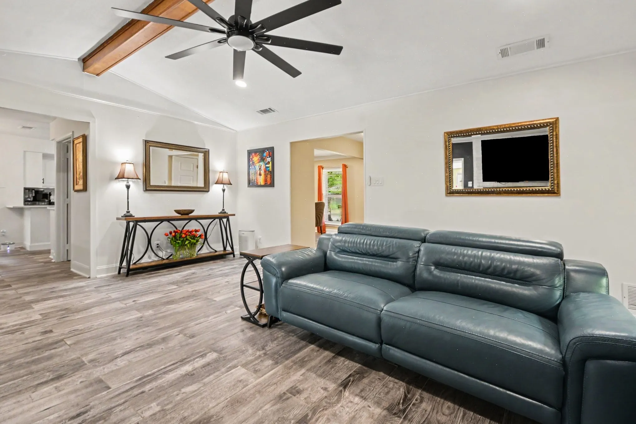 Vaulted ceiling with exposed wood beam, contemporary ceiling fan, wood-finish flooring, and white walls