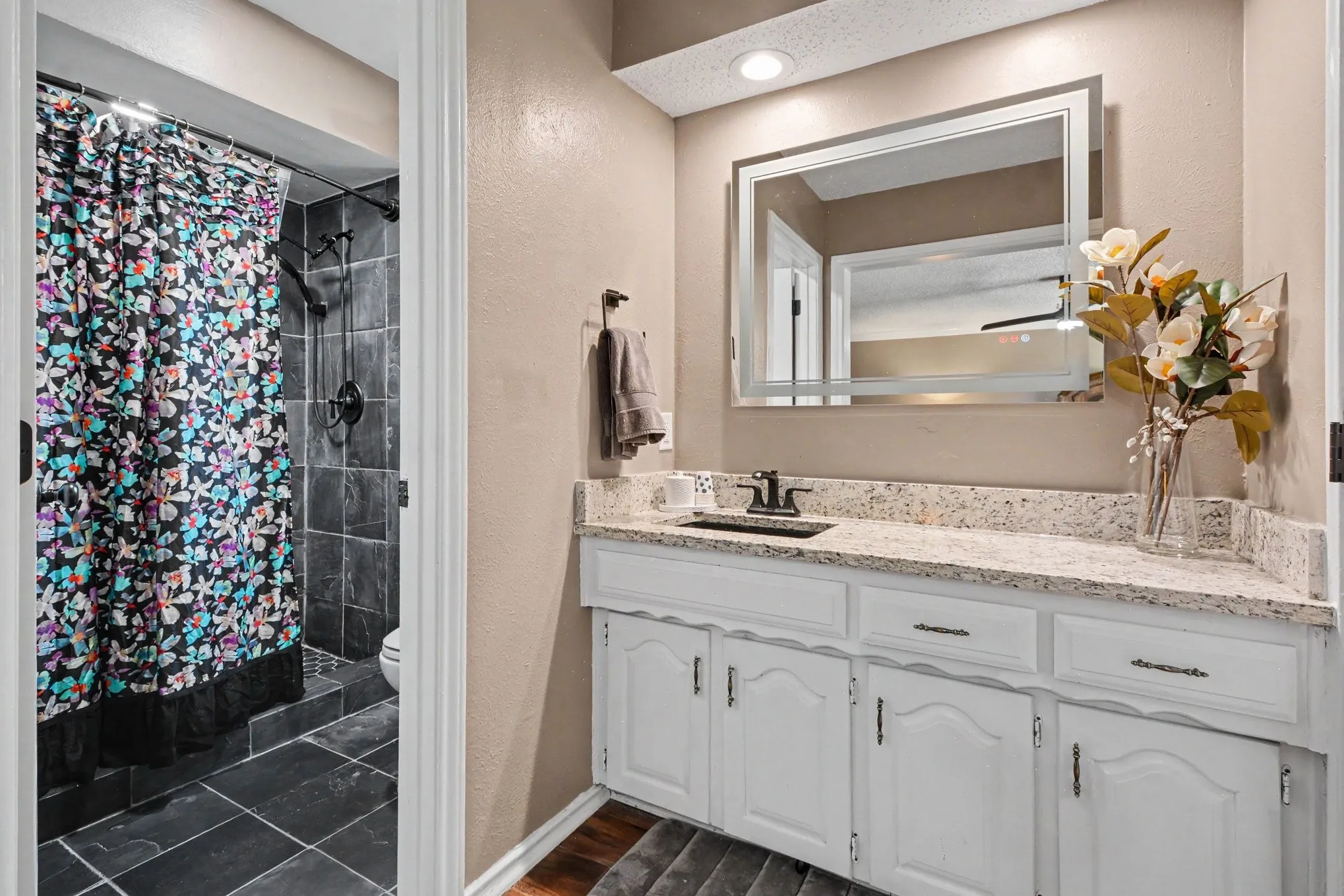 Vanity with a light-colored countertop, white cabinetry with dark hardware, and a framed mirror with integrated lighting