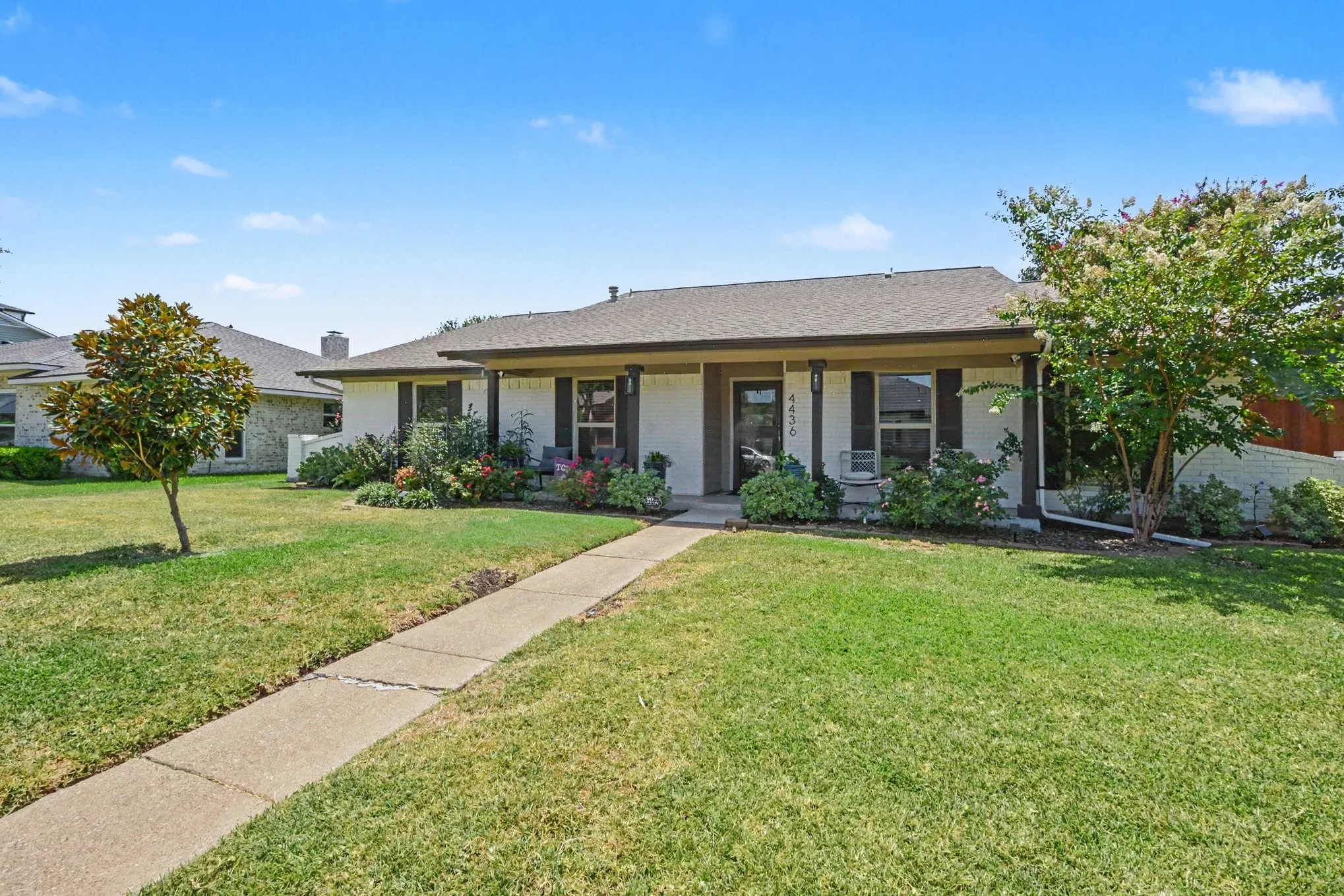 Welcoming front exterior with covered porch, mature landscaping, and a broad lawn.