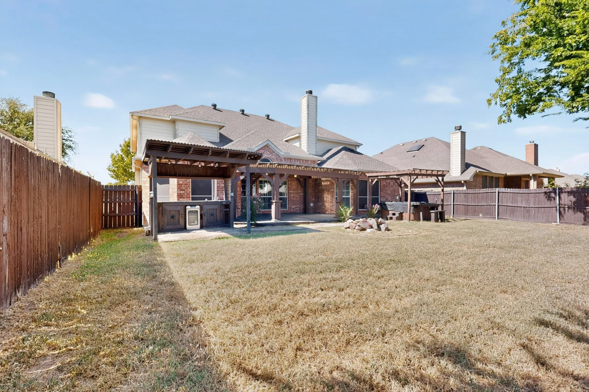 Expansive backyard featuring a built-in outdoor kitchen, multiple pergolas, and a fenced perimeter