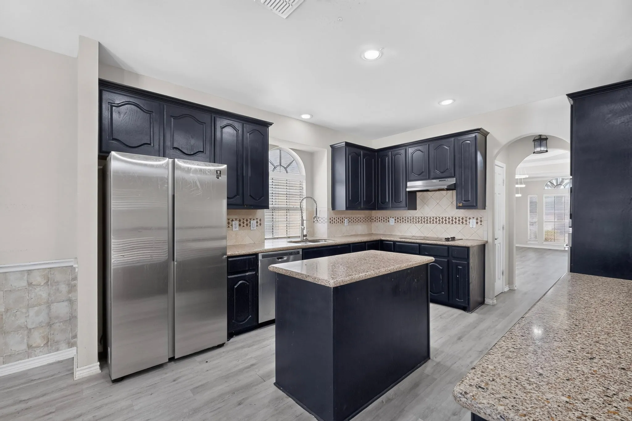 Kitchen featuring dark cabinetry, light-toned countertops, a center island, stainless steel appliances, and light wood-finish​​‌​​​​‌​​‌‌​‌‌​​​‌‌​‌​‌​‌​​​‌​​ flooring