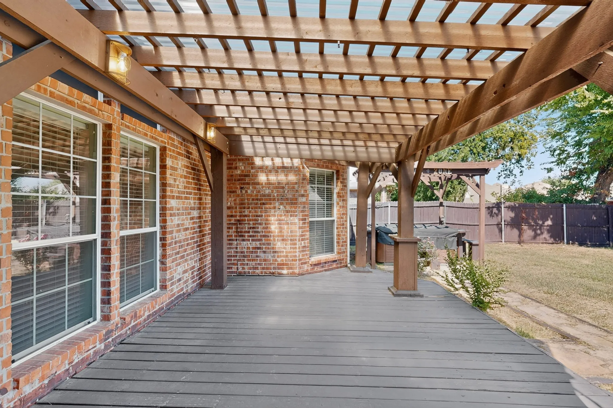 Expansive outdoor deck featuring dark wood-finish planking, an overhead pergola with translucent panels, and integrated lighting fixtures