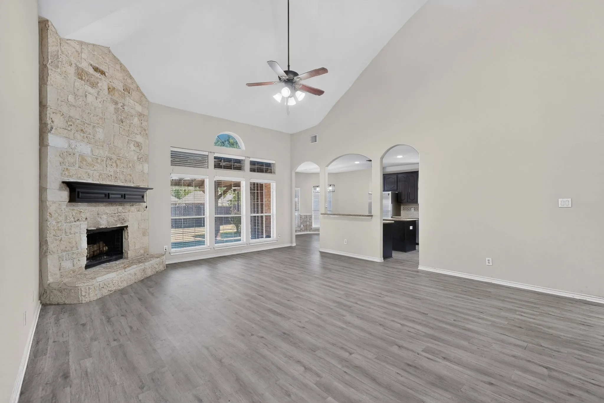 Spacious open-concept living area featuring soaring vaulted ceilings, ceiling fan with integrated lighting, and wood-finish flooring throughout