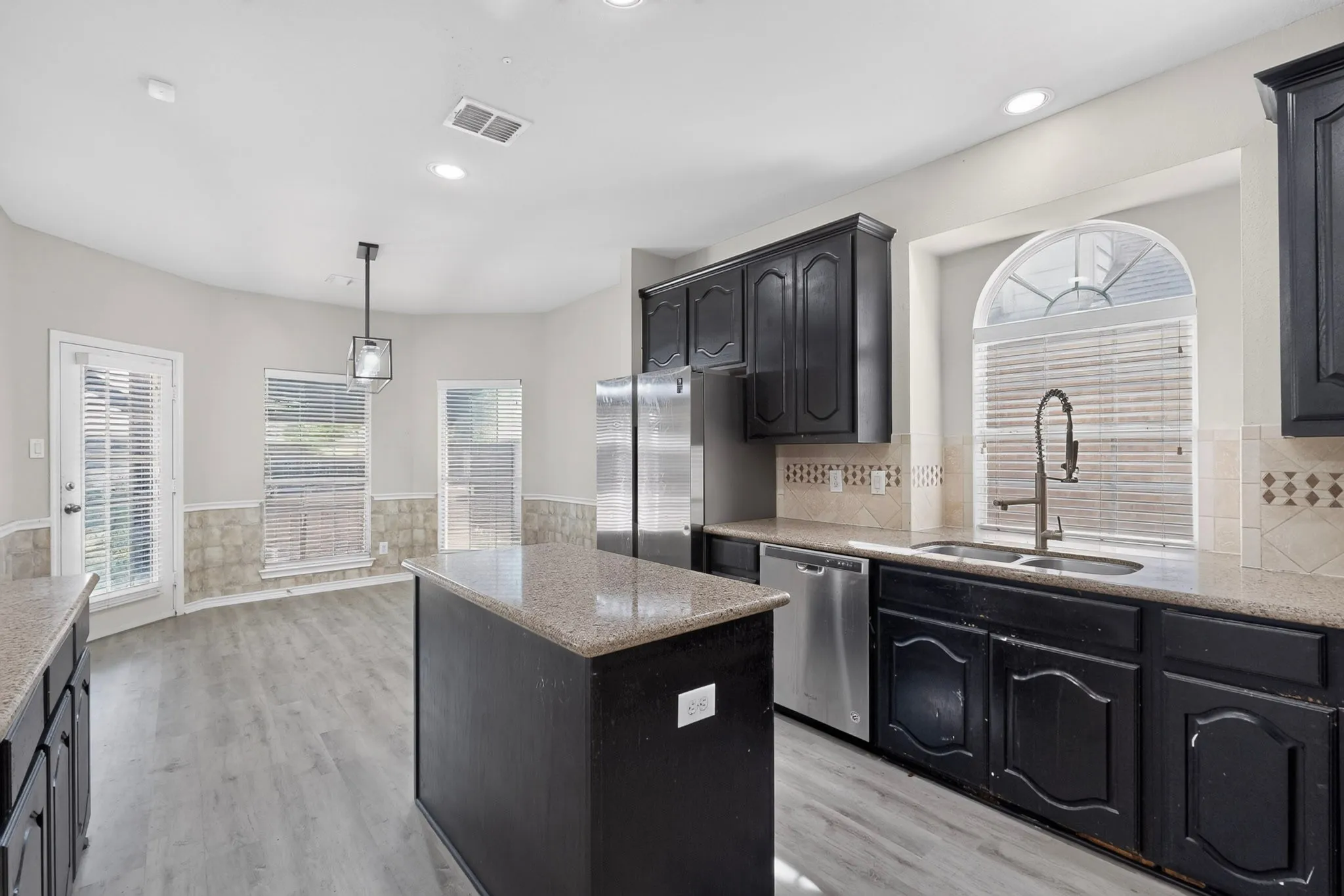 Kitchen featuring wood-finish flooring, dark cabinetry, stone countertops, and a tile backsplash