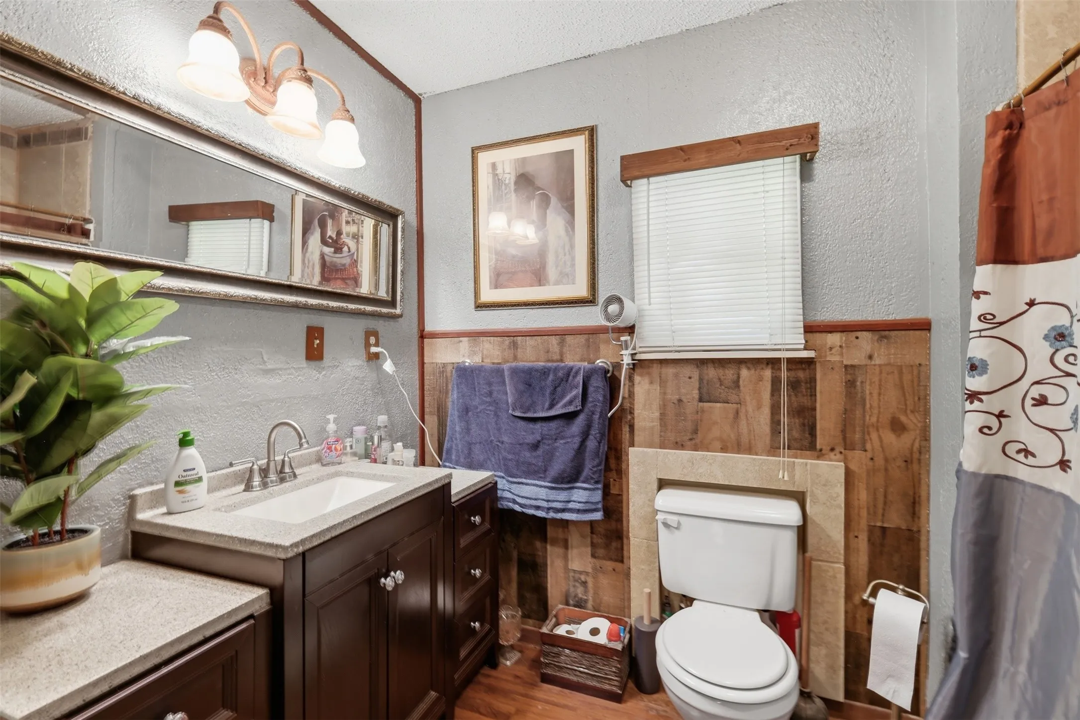 Secondary bathroom featuring a double vanity, wood wainscoting, framed mirrors, and toilet.