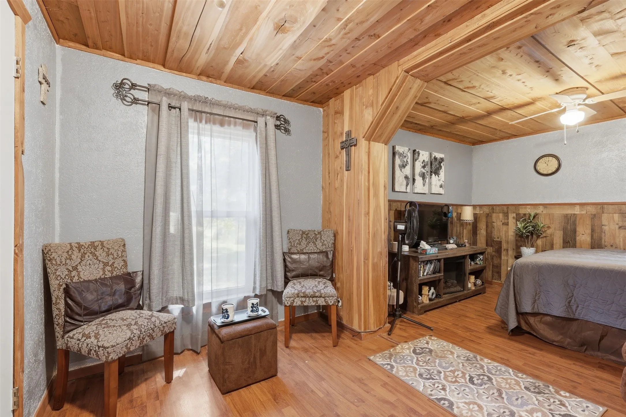 Rustic bedroom featuring warm wood plank ceilings, wainscoting, window lighting, and plush seating setup.