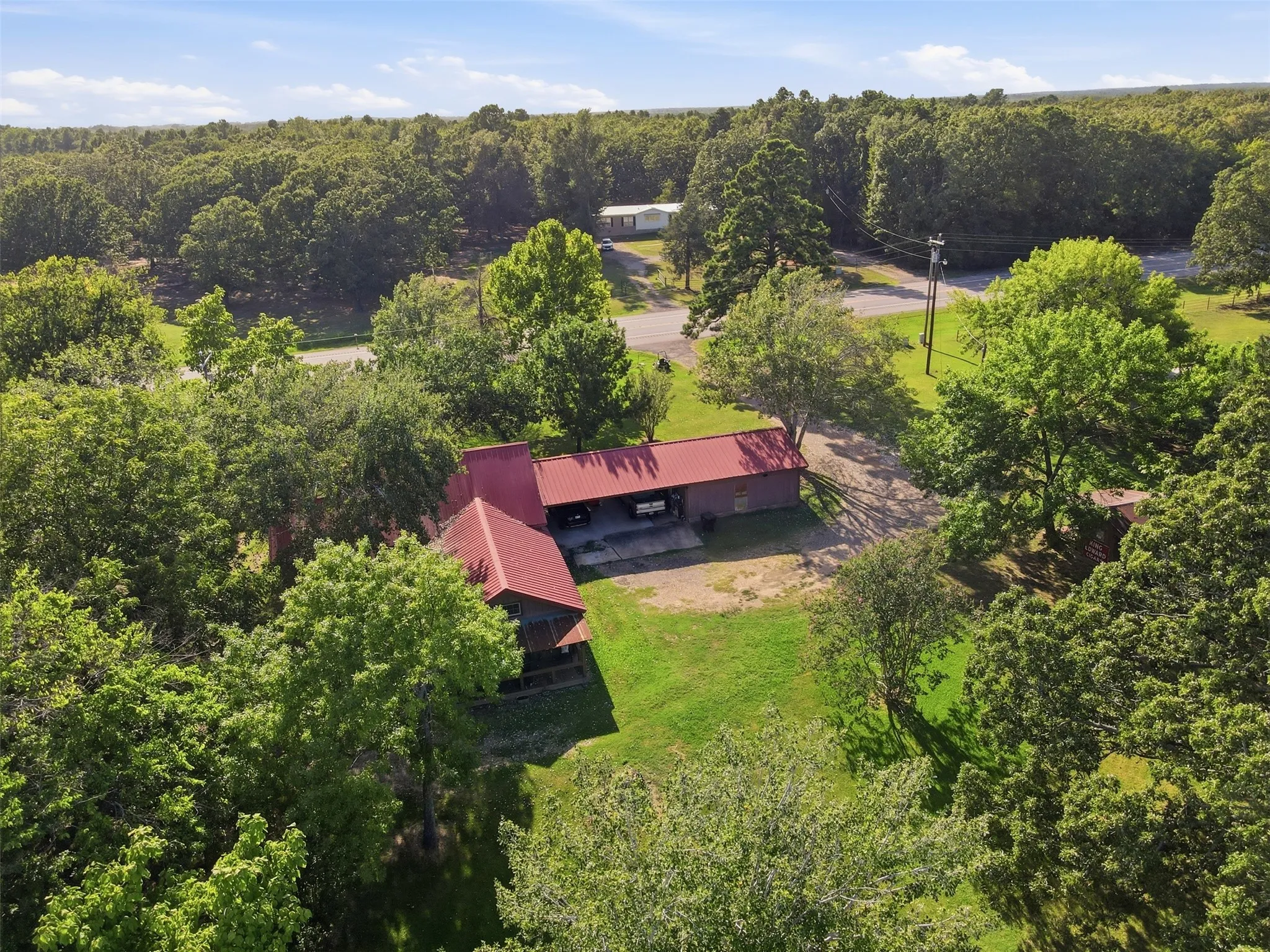 Bird’s-eye aerial view framing the red roof profile of the home nestled within a thick grove of mature trees.
