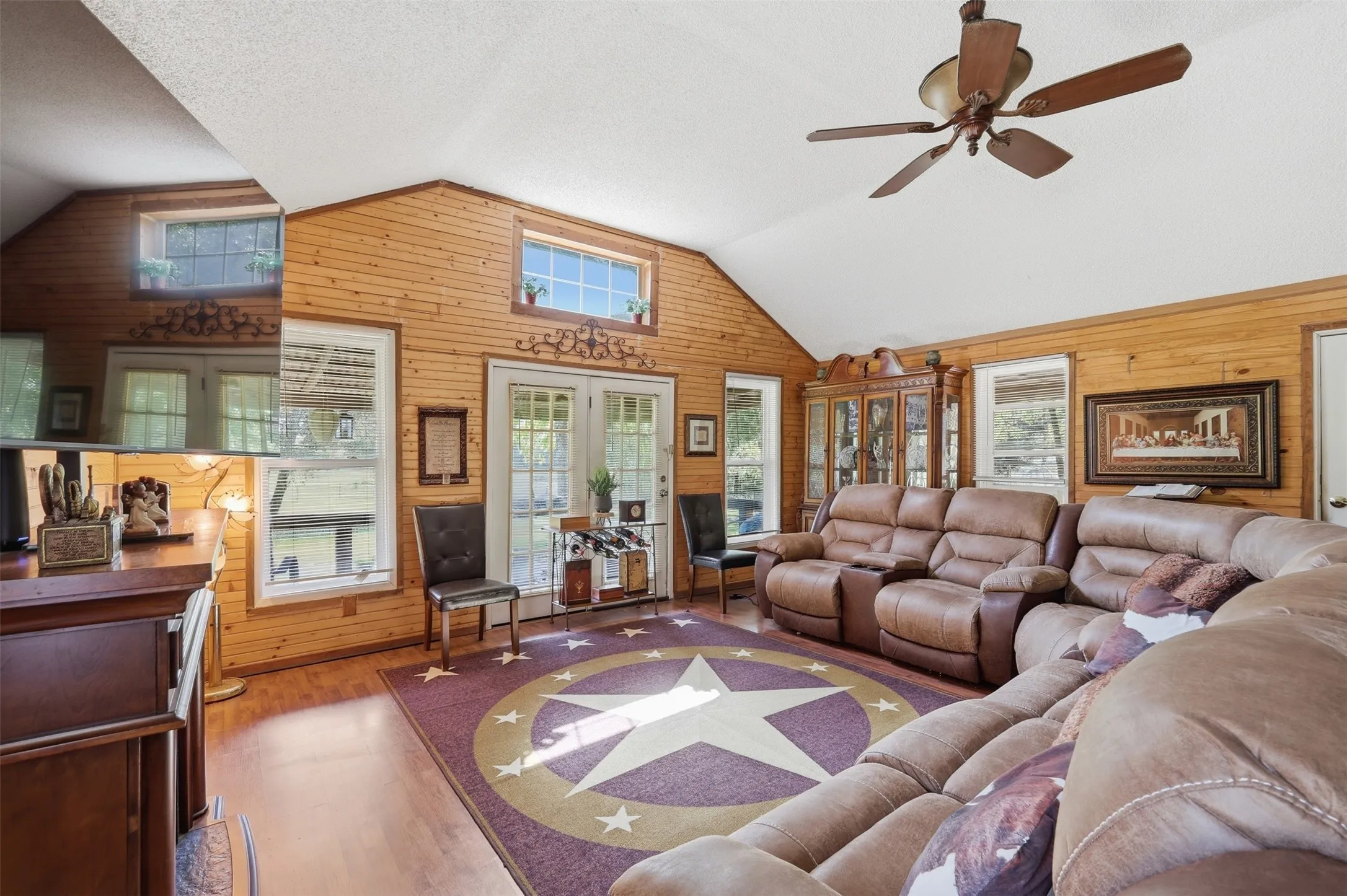 Expansive main living room featuring vaulted wood-paneled ceilings, ceiling fan, rustic wall finishes, and ample seating space.
