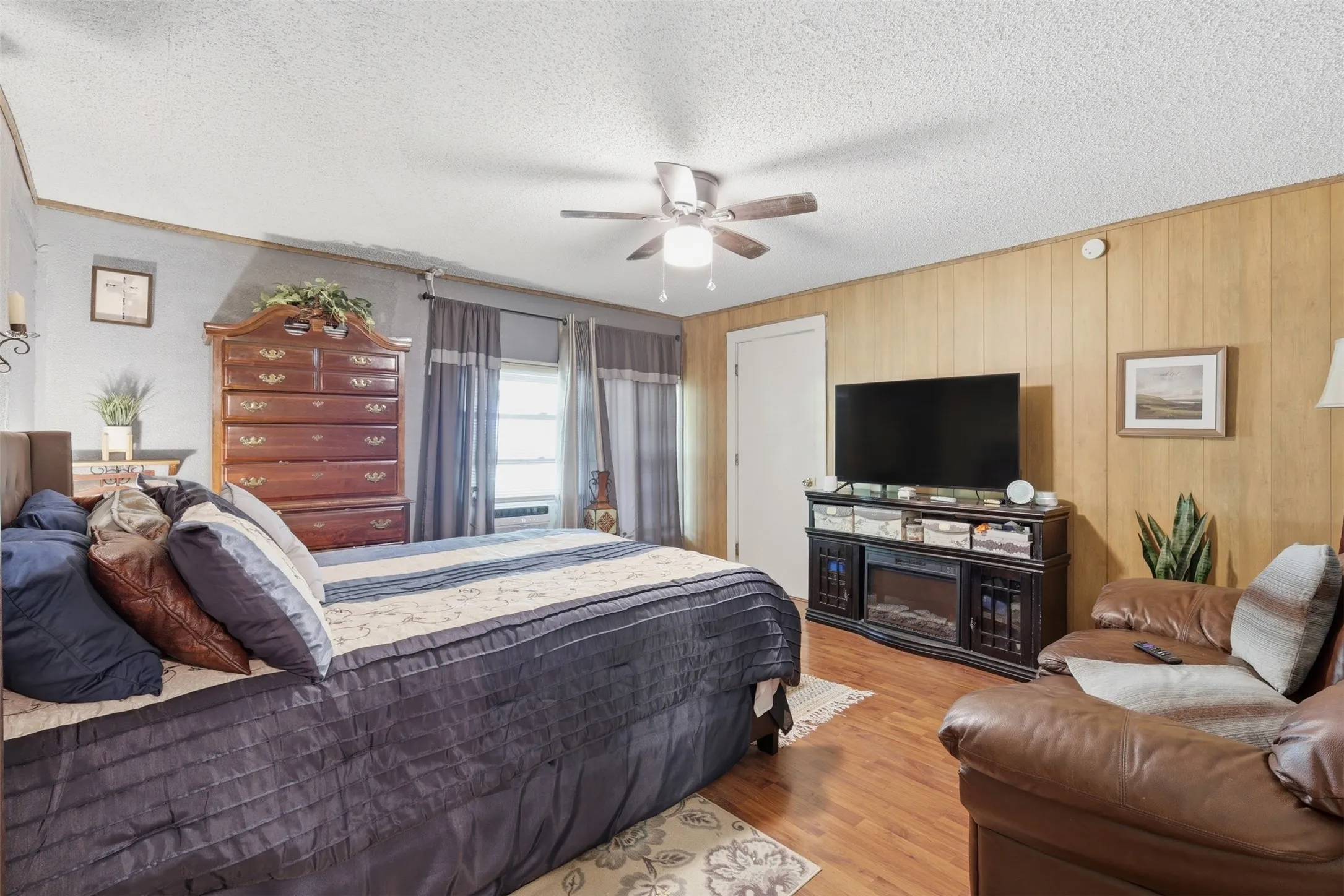 Comfortable bedroom offering wood-panel accent wall, ceiling fan, and space for a full furniture set.