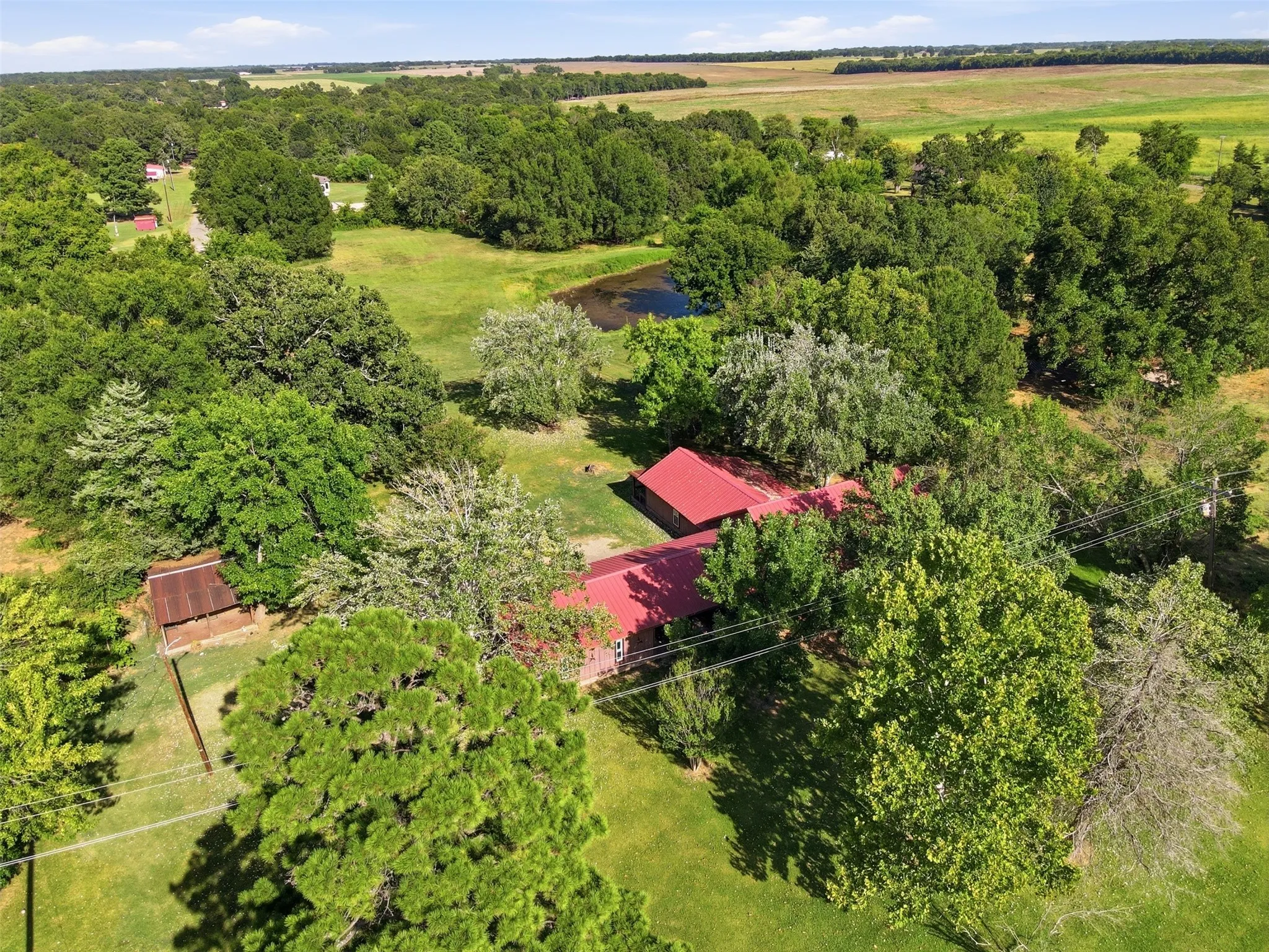 Broad aerial view showing the home site, private pond, and surrounding open acreage.
