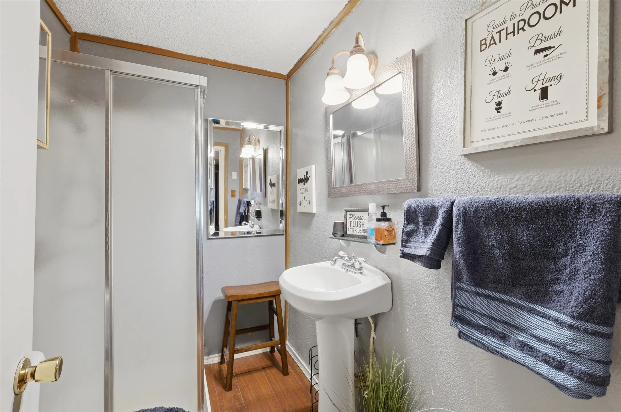 Full bathroom equipped with a pedestal sink, framed wall mirror, walk-in shower, and bright lighting.