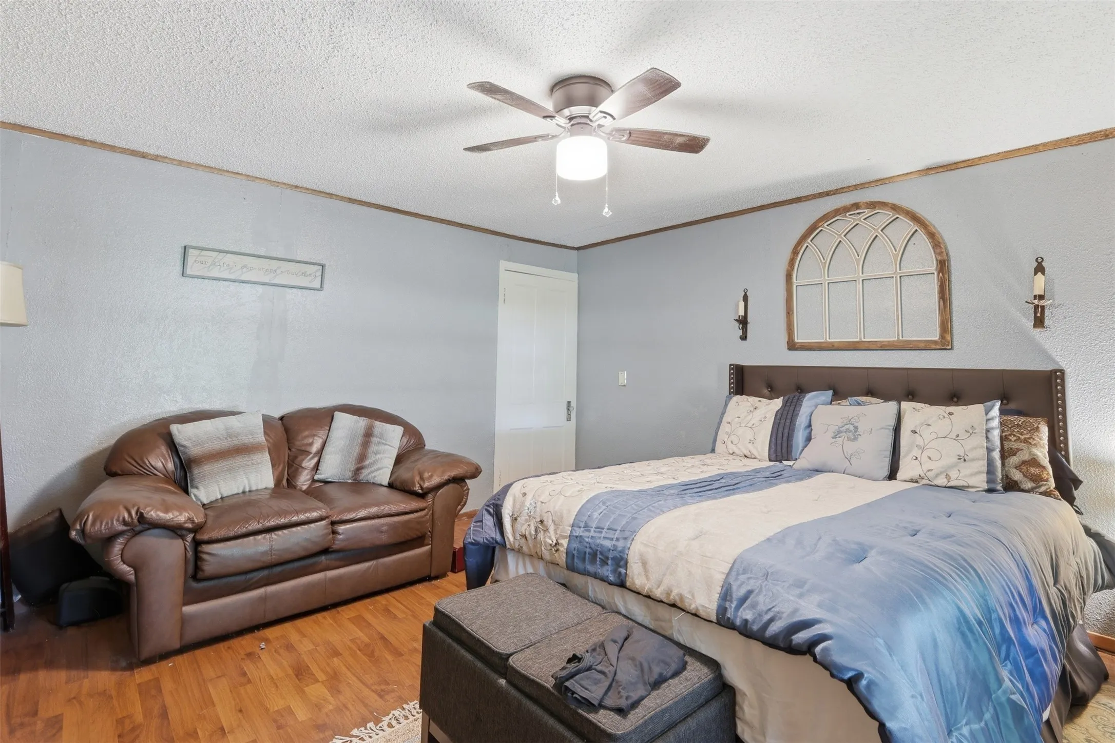 Primary bedroom suite featuring soft wall tones, ceiling fan, and comfortable seating area.