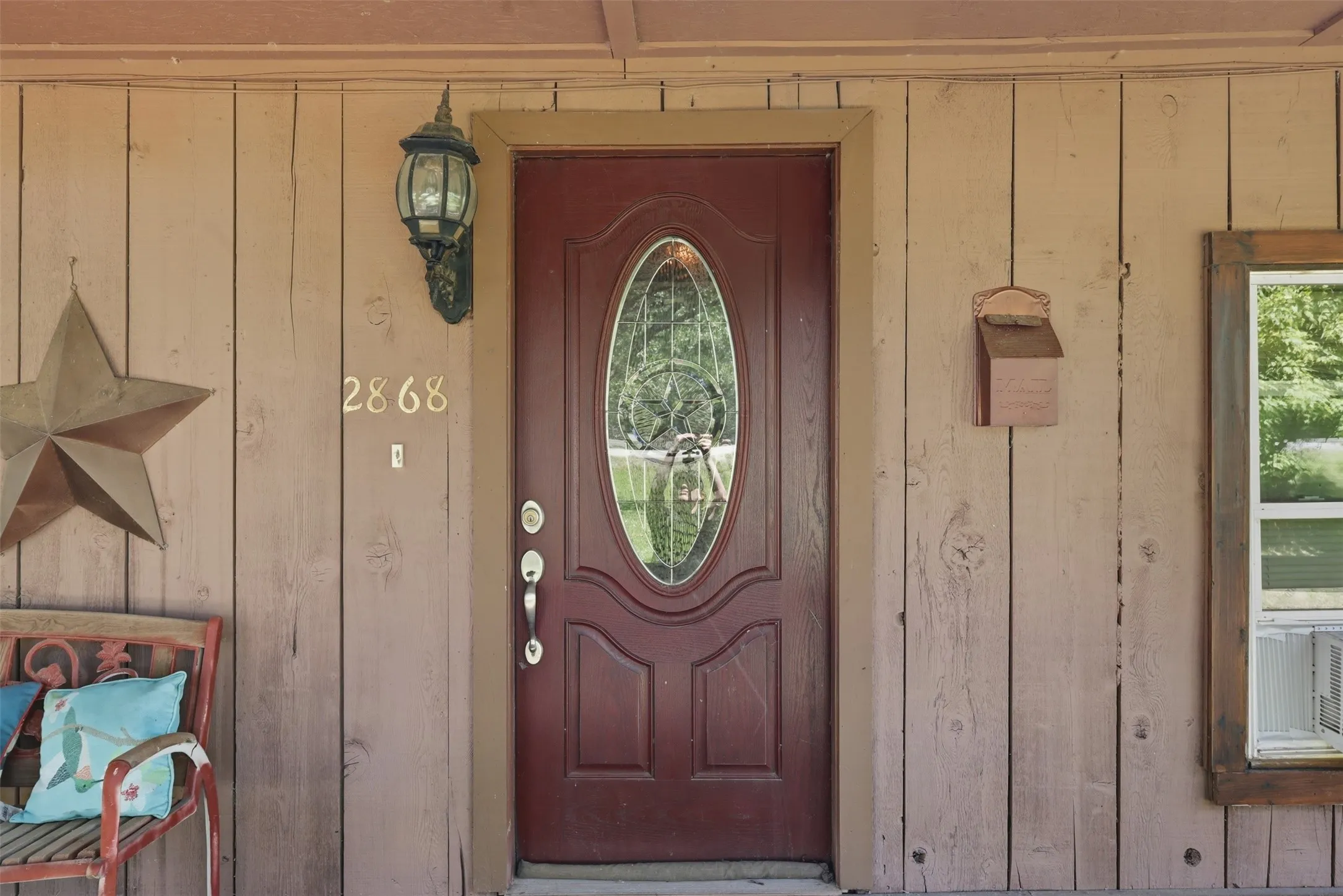 Front entryway close-up showing the wooden door with decorative glass oval insert and rustic wood siding.