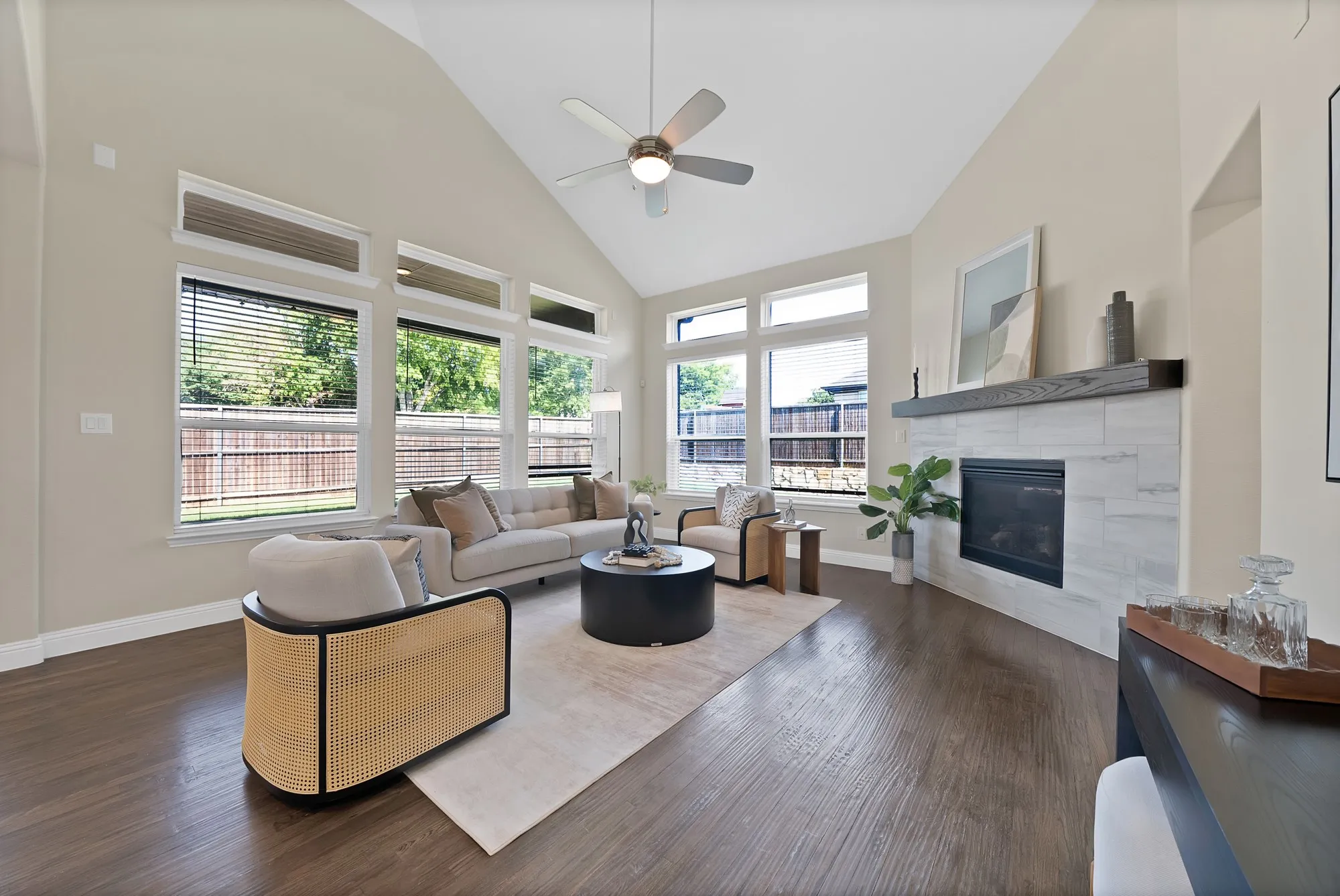Vaulted ceiling with a ceiling fan, dark wood-finish flooring, and a fireplace with a light-colored tile surround and wood mantel