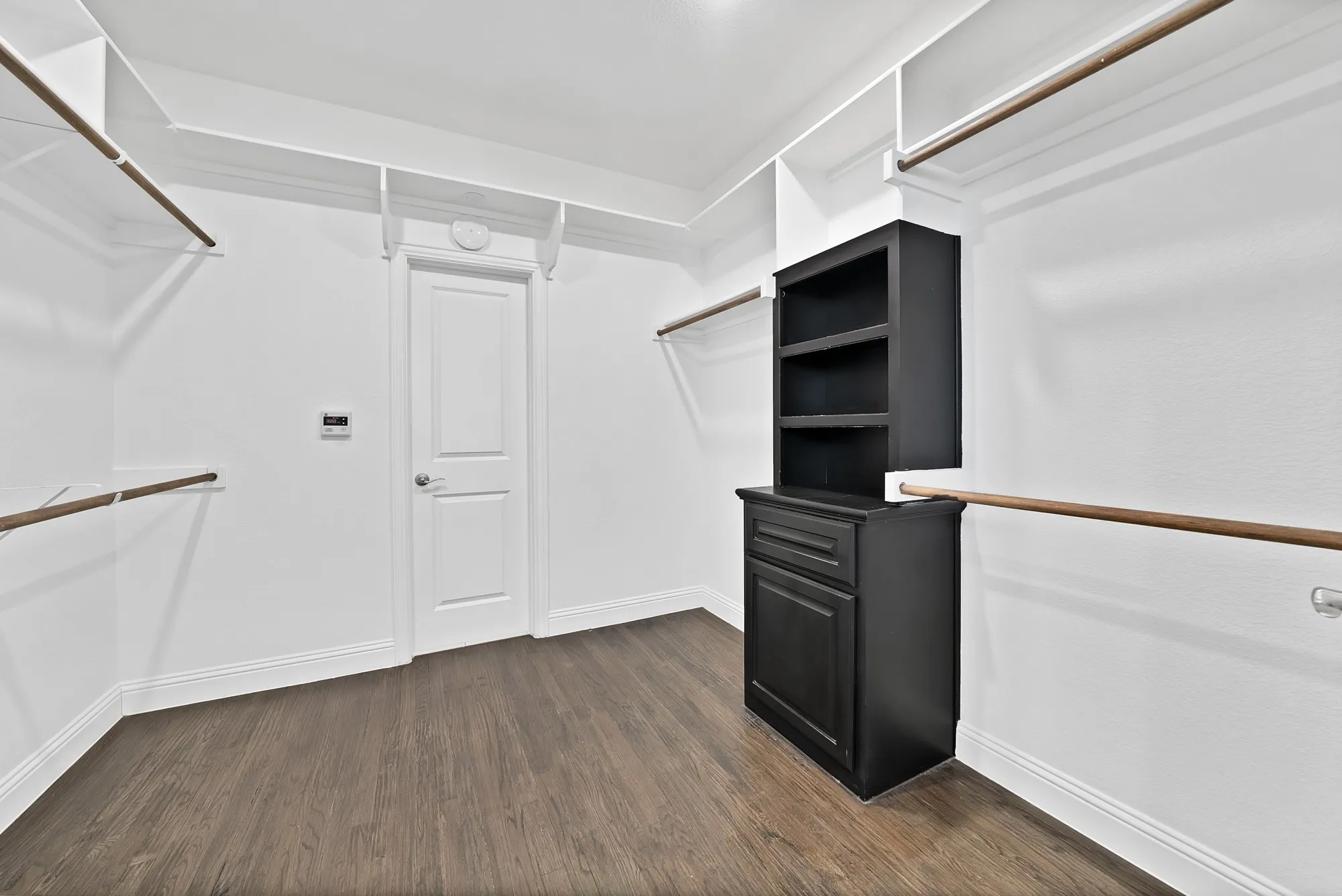Expansive walk-in closet featuring wood-finish flooring, white shelving, and wooden hanging rods