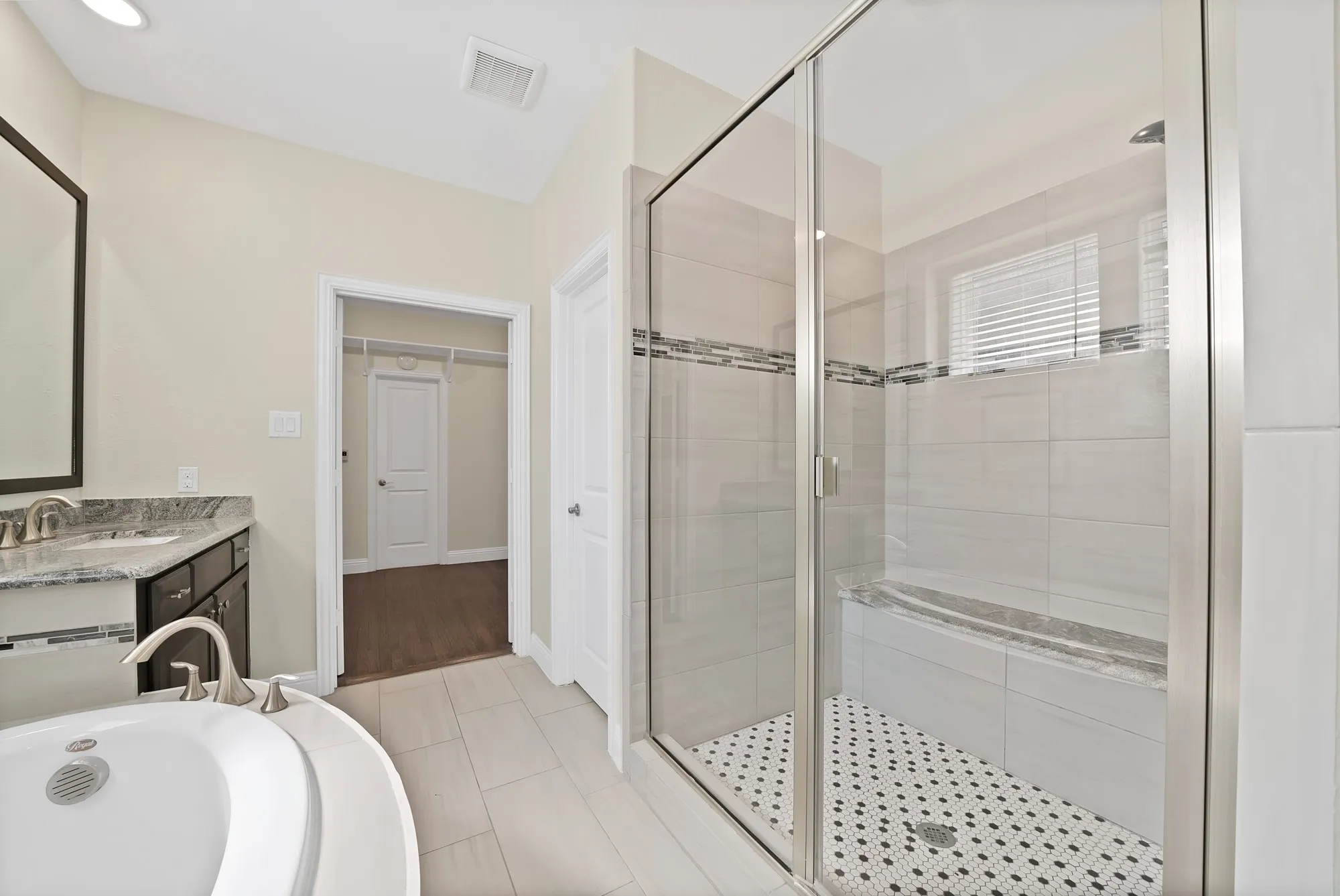 Spacious bathroom with a walk-in shower featuring a tiled bench, a soaking tub, a vanity with a stone countertop, and tile flooring