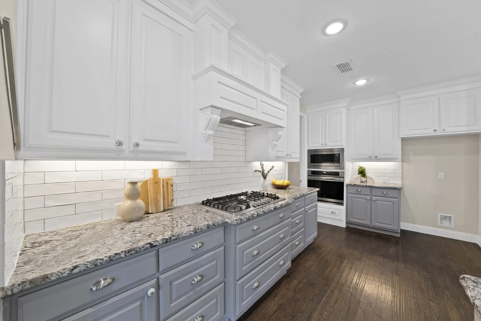 White upper cabinetry, gray lower cabinetry, light-toned countertops, subway tile backsplash, and dark wood-finish flooring