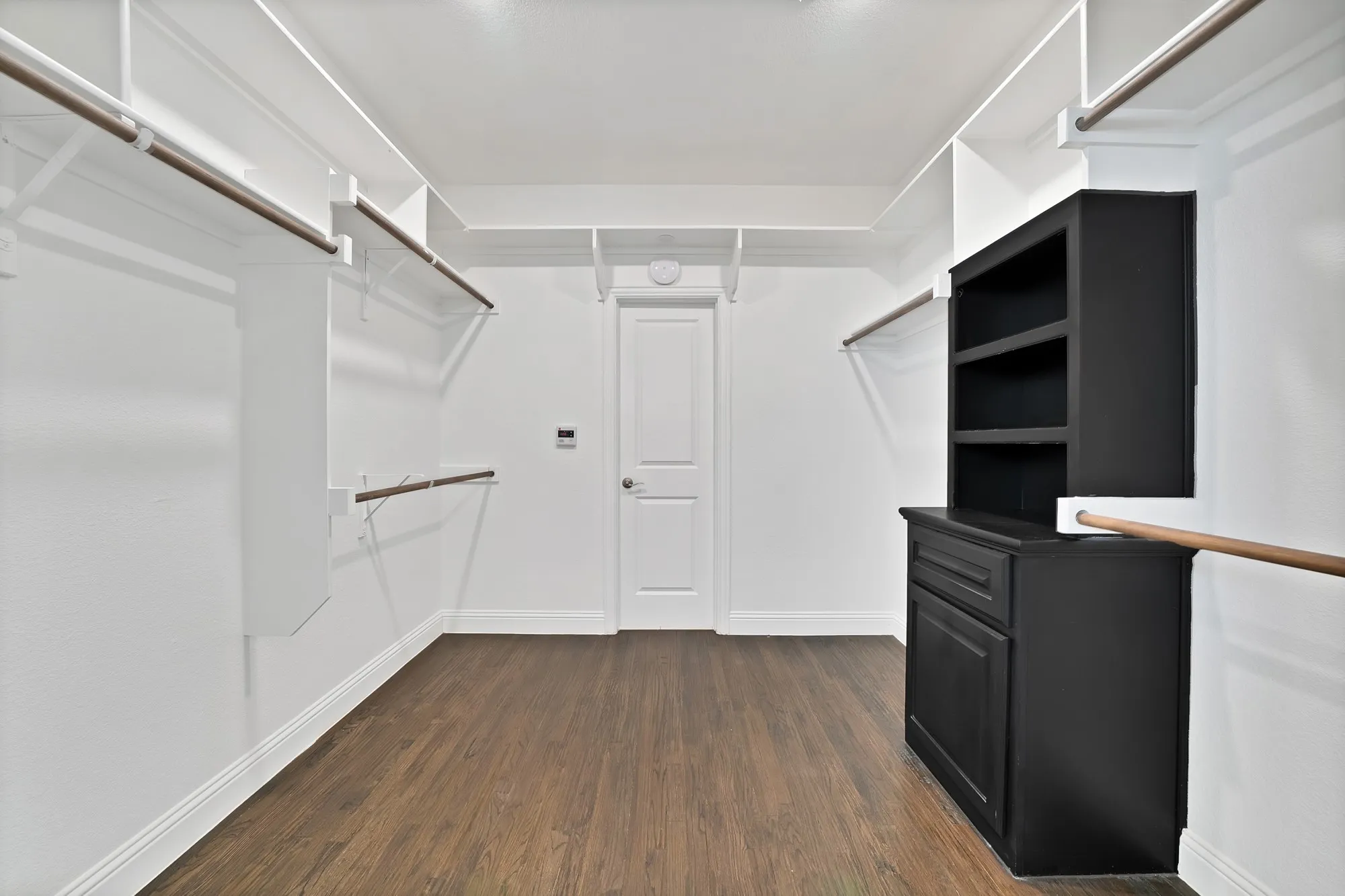 Wood-finish flooring, white built-in shelving, multiple hanging rods, and a black built-in storage cabinet with shelving