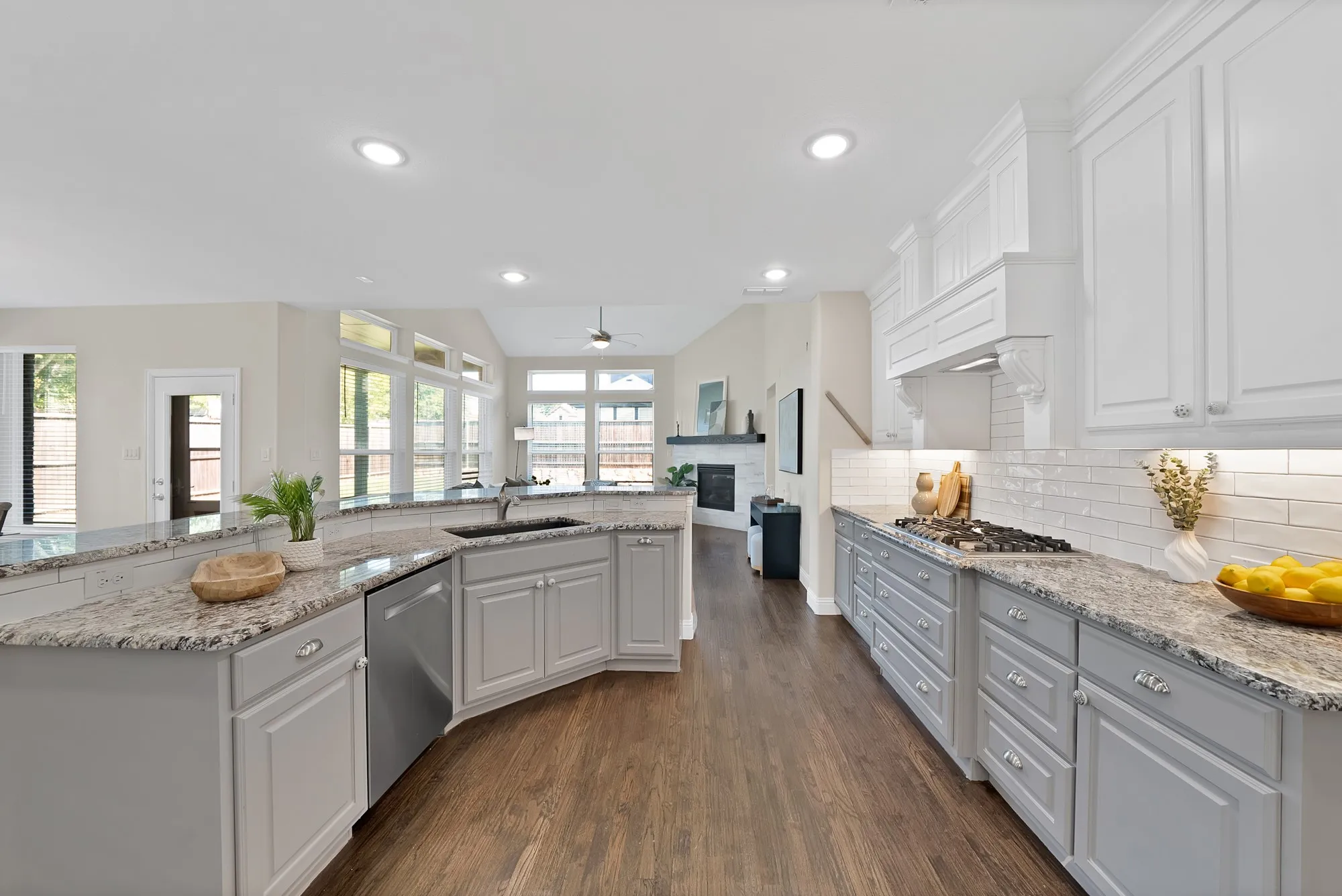 Spacious kitchen featuring granite countertops, stainless steel dishwasher, white subway tile backsplash, and wood-finish flooring