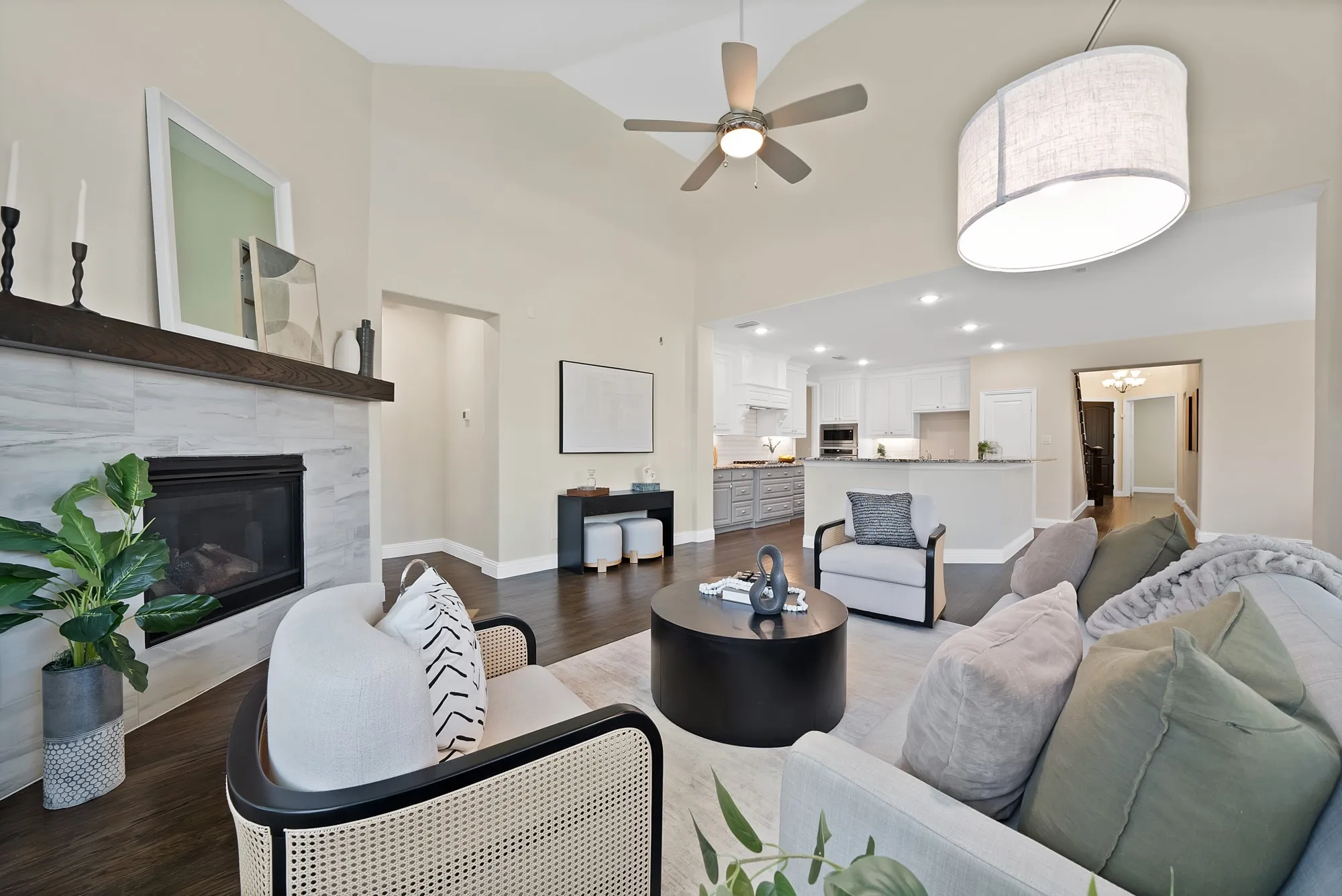 Vaulted ceiling with a ceiling fan, fireplace with a wood mantel and tile surround, recessed lighting, wood-finish flooring, and a kitchen with white cabinetry