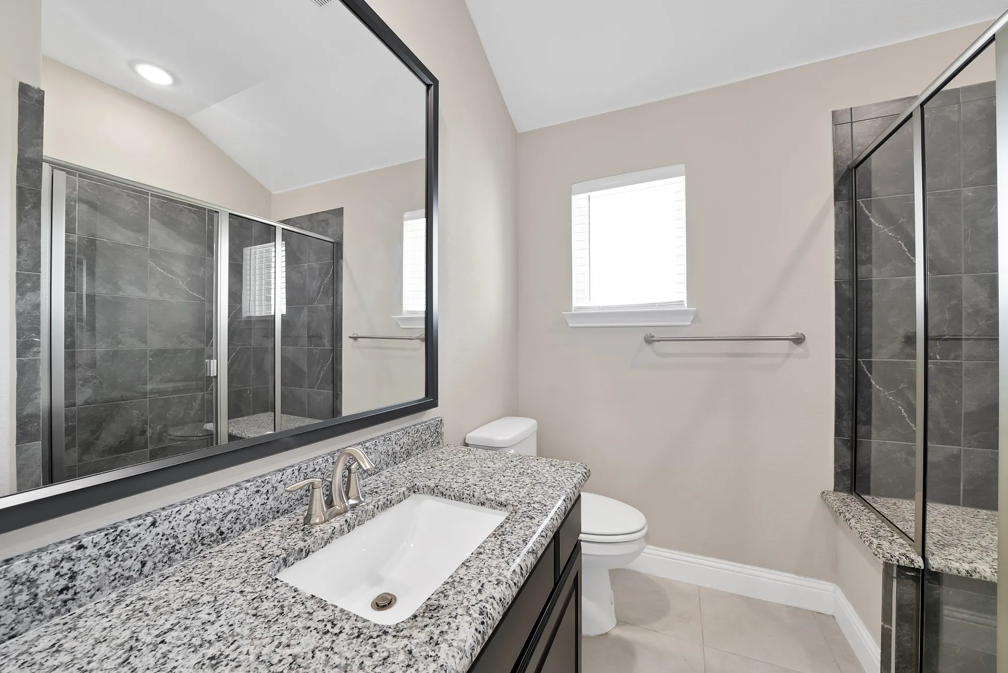 Granite countertop vanity with integrated sink, framed mirror, fully tiled shower with glass enclosure, tiled flooring, and a window with blinds