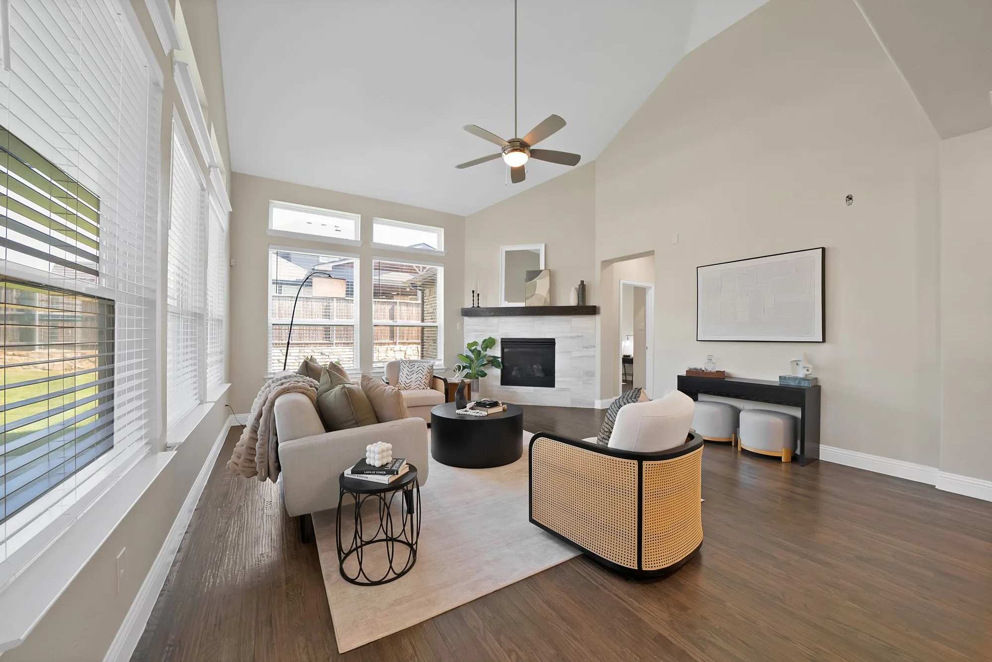 Vaulted ceiling with an attached ceiling fan, floor-to-ceiling windows, wood-finish flooring, and a fireplace with a wood mantel