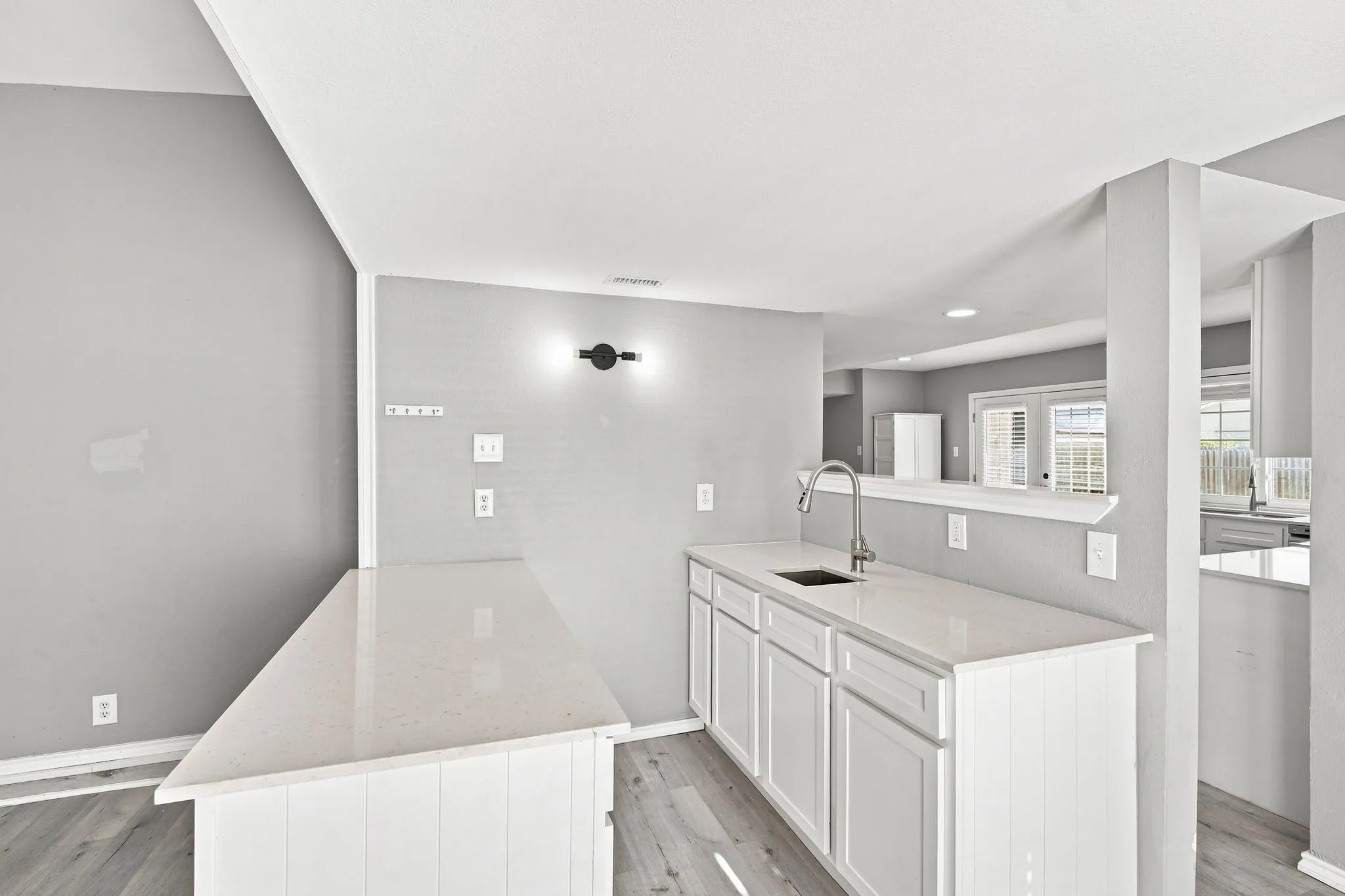 Kitchen featuring white cabinetry, light-toned countertops, a stainless steel gooseneck faucet, and wood-finish flooring