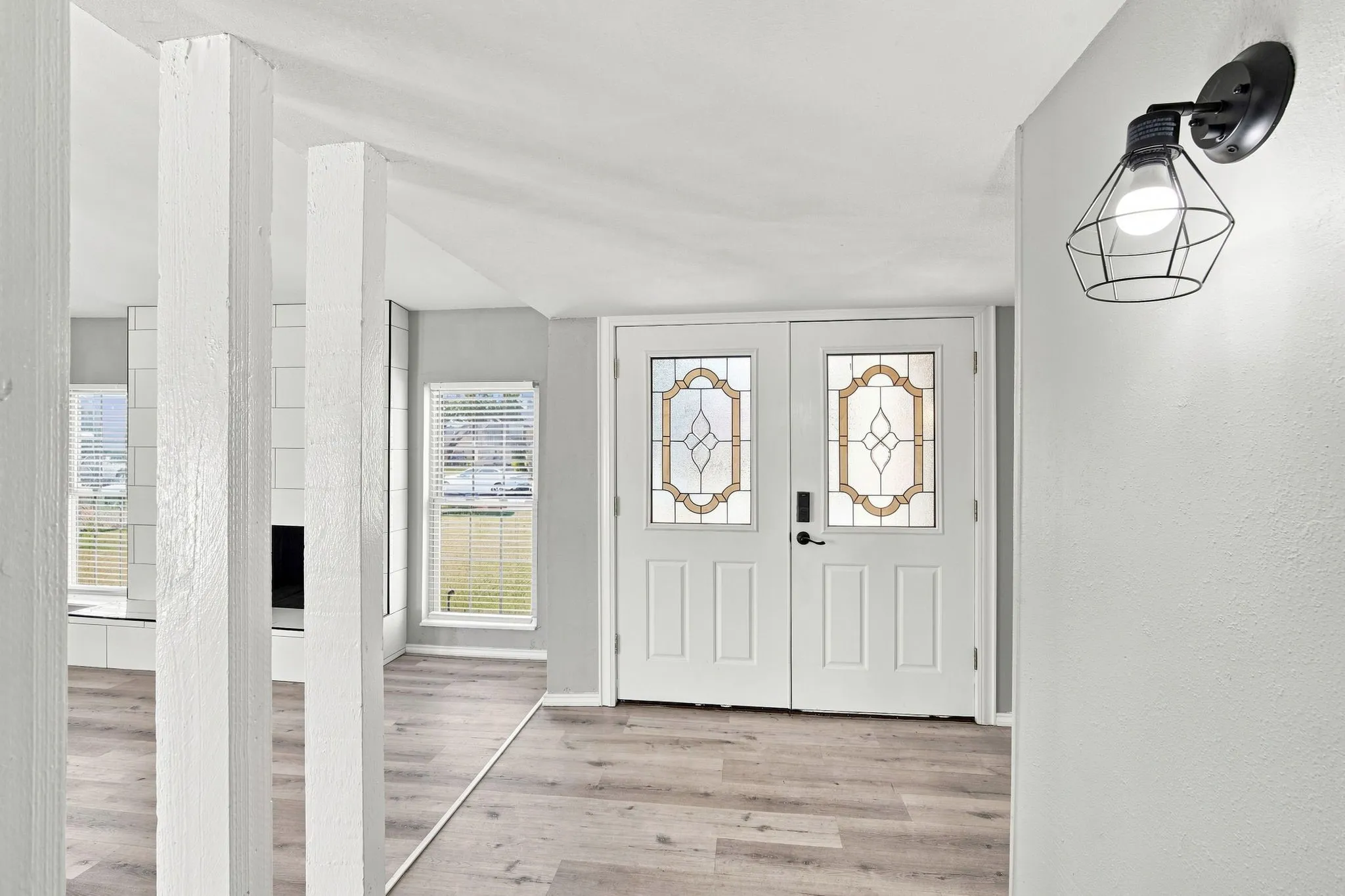 Double entry doors with decorative glass panels, wood-finish flooring, and a modern wall sconce