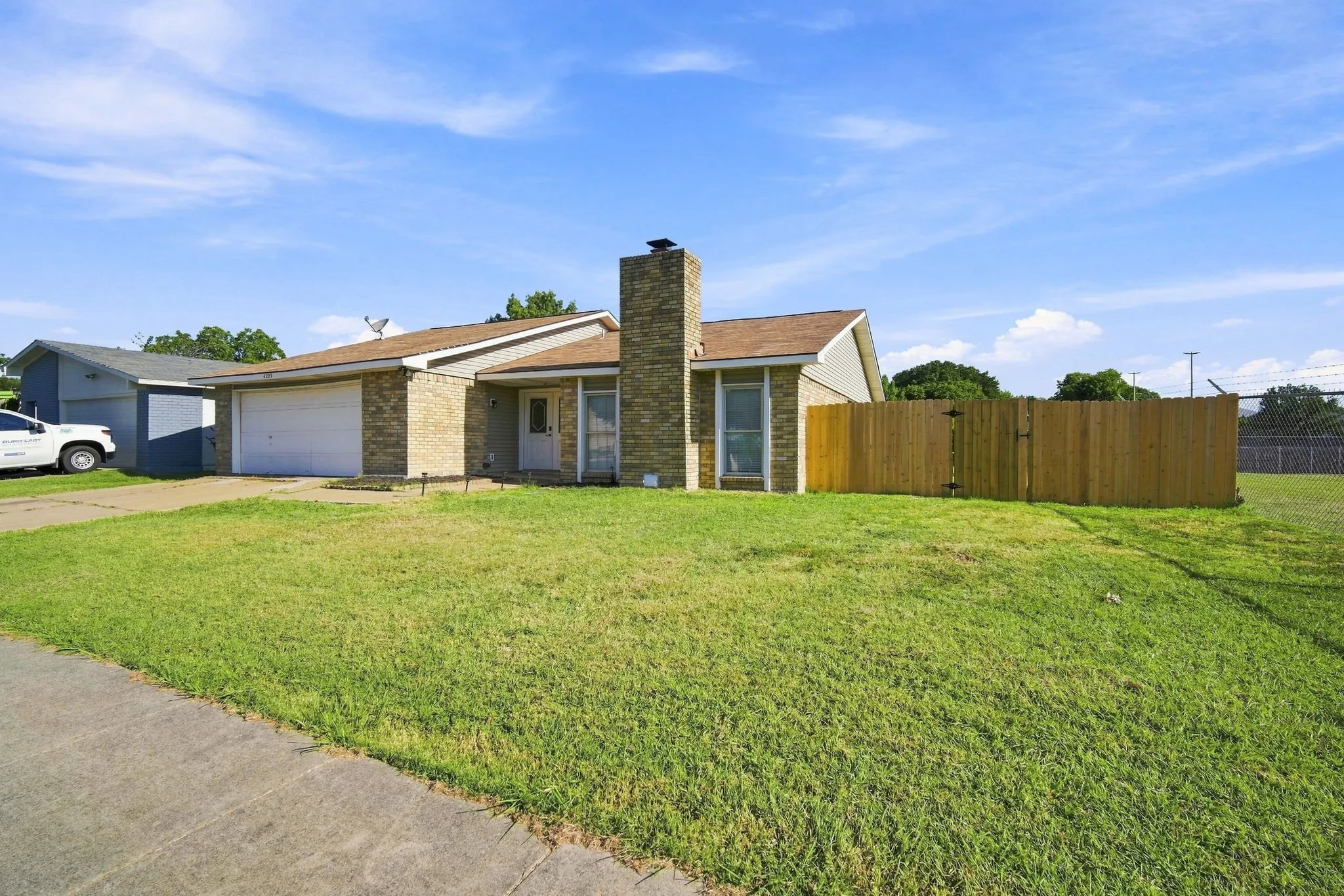 Brick exterior with an attached garage, a prominent brick chimney, and a wooden privacy fence