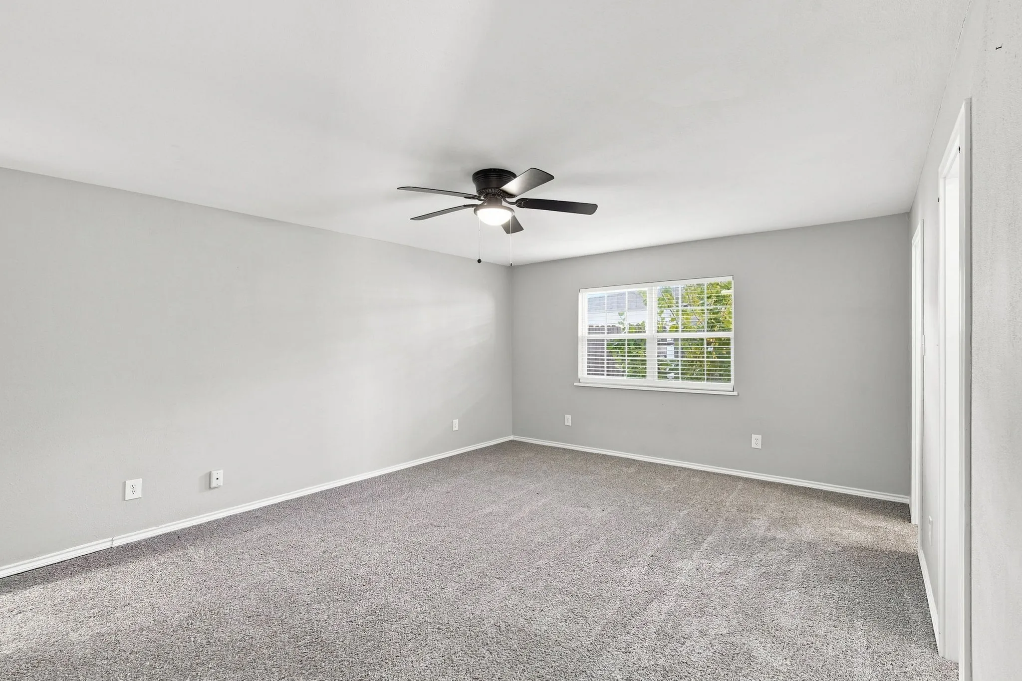 Spacious room featuring neutral carpeting, a ceiling fan with integrated lighting, a large window with horizontal blinds, and light-toned walls
