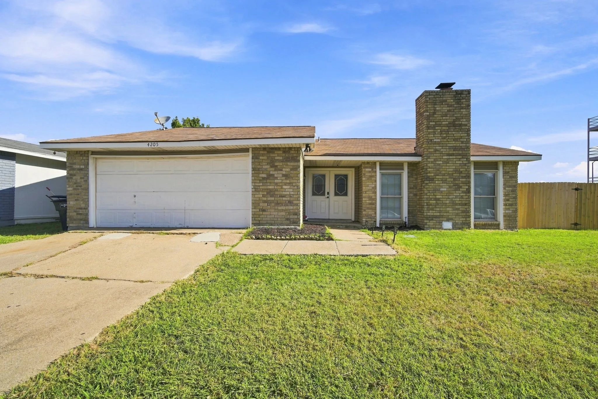 Brick exterior with a prominent chimney feature, an attached garage, a walkway leading to a double-door entry, and a wood fence enclosing the side yard