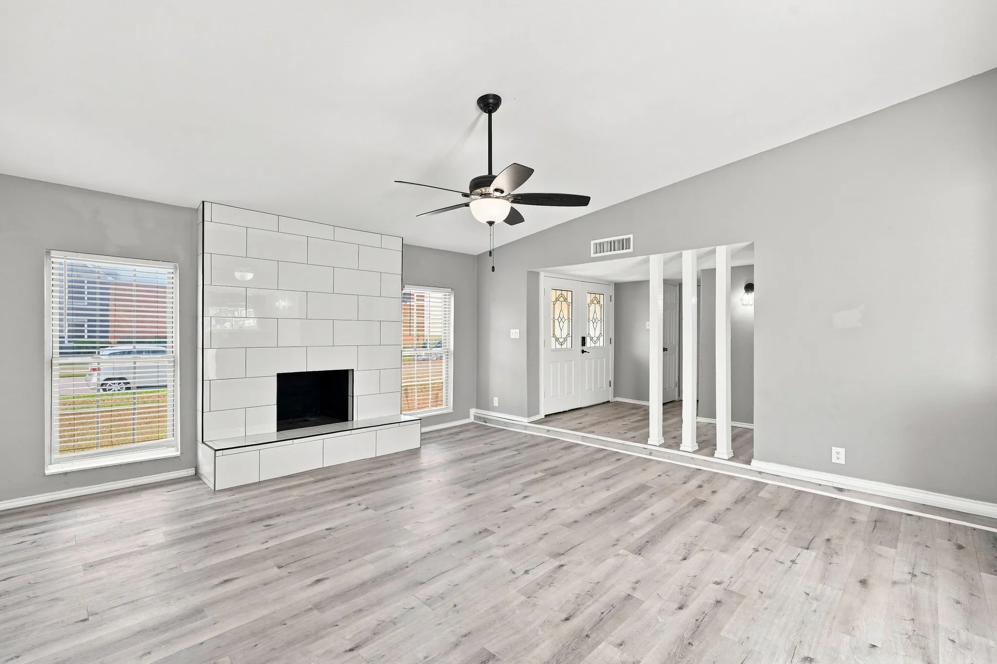 Spacious living area featuring wood-finish flooring, a white tiled fireplace, and a ceiling fan with integrated lighting